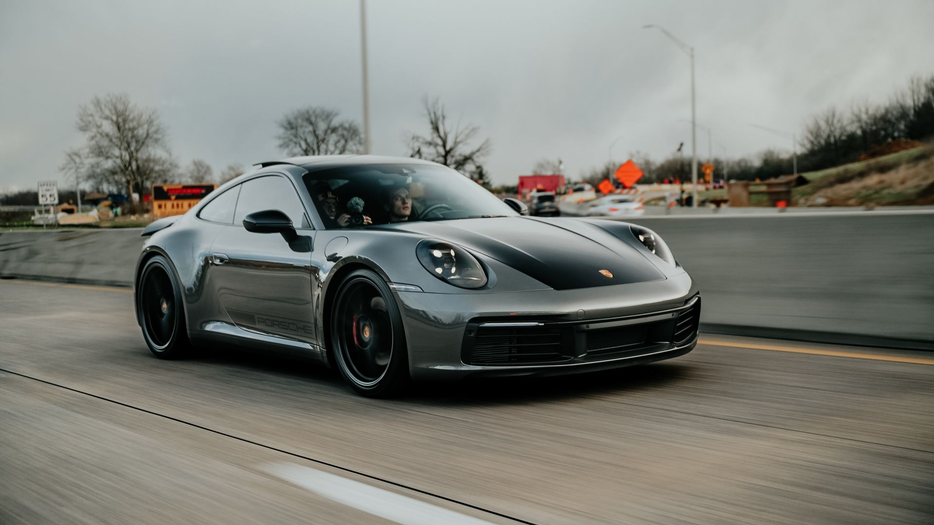 A silver porsche 911 is driving down a highway.