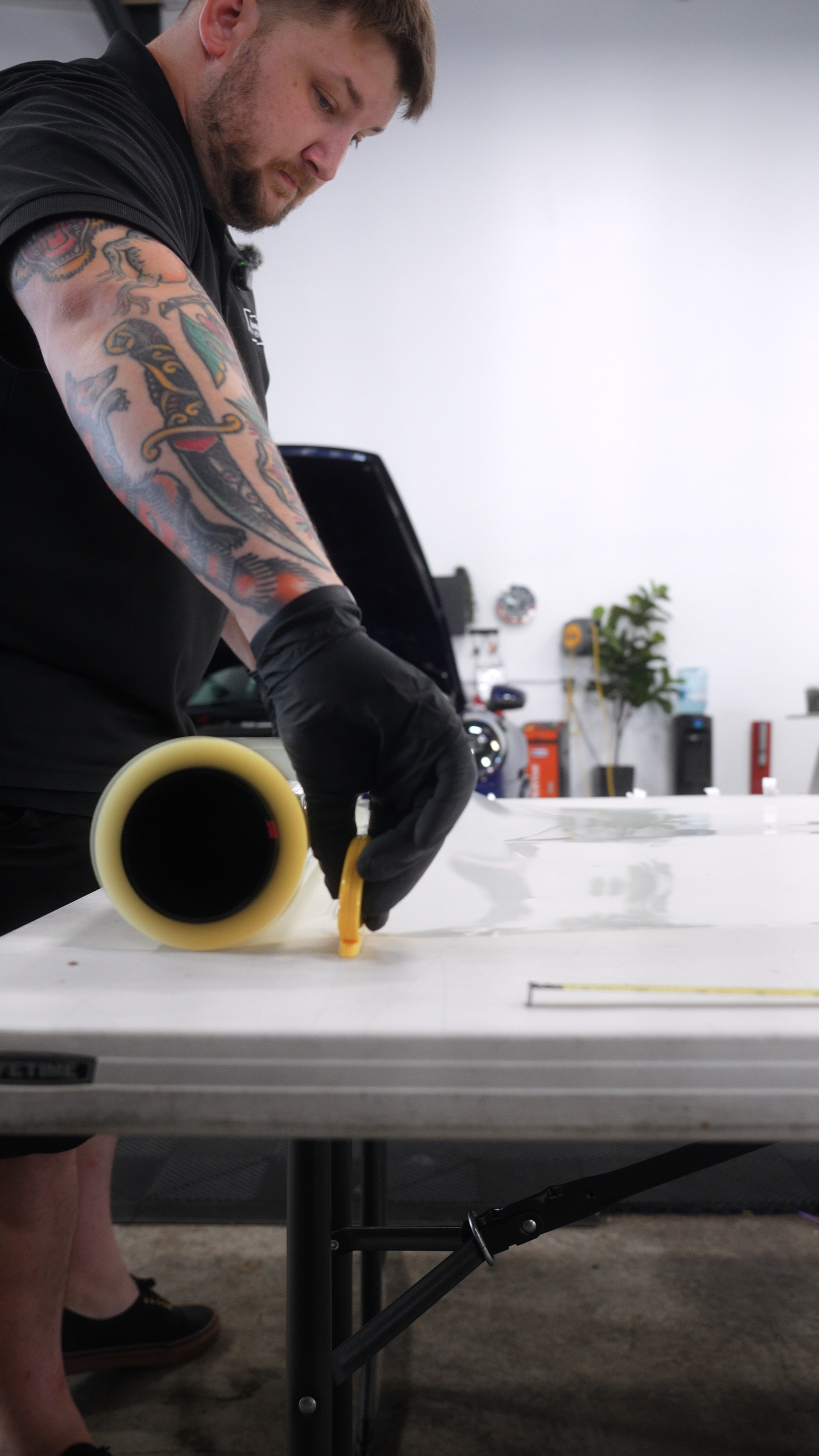 Man in black gloves cutting film on a table; black film roll and white surface visible.
