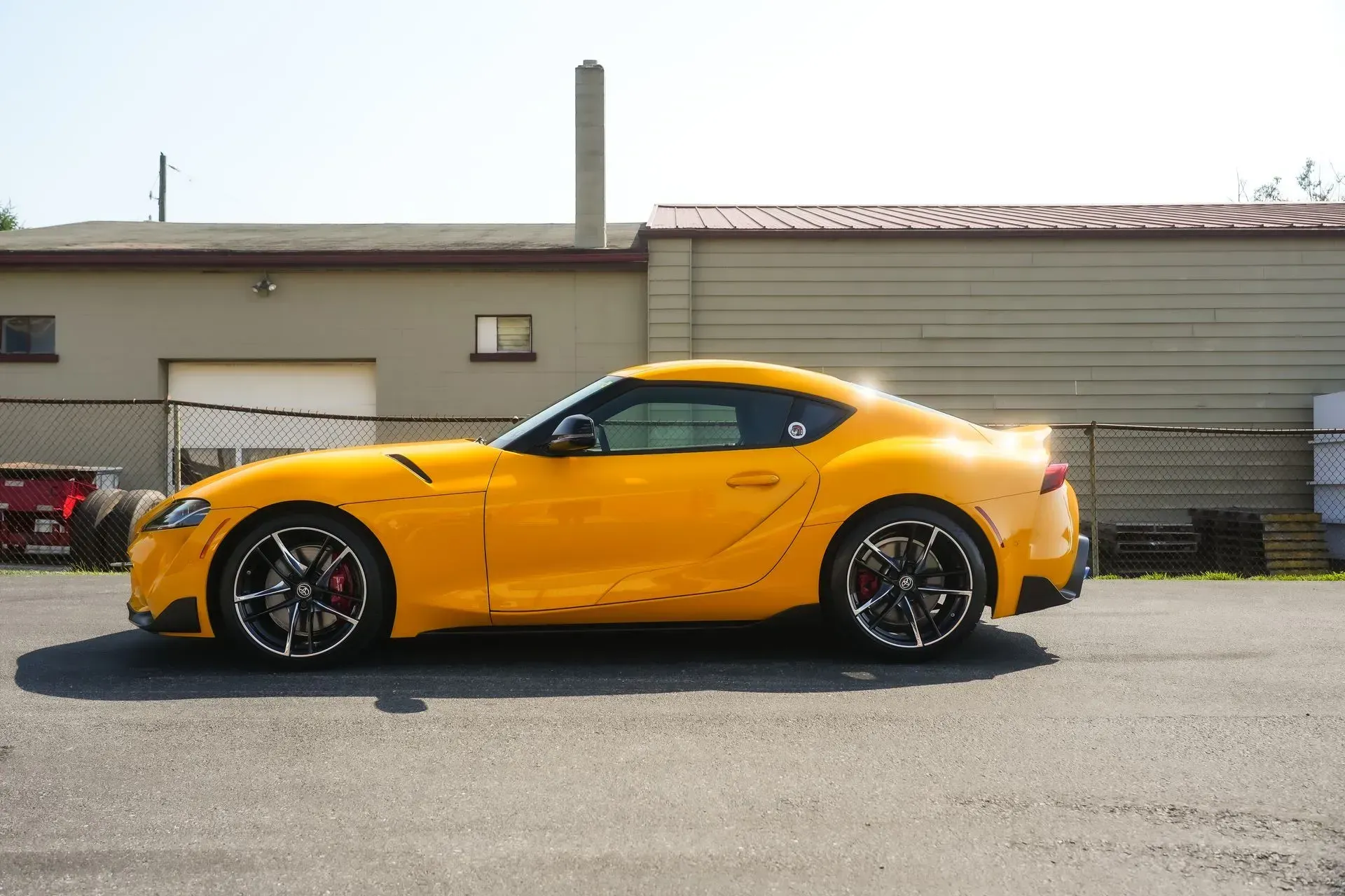 Yellow Toyota Supra sports car parked near a building on a sunny day.
