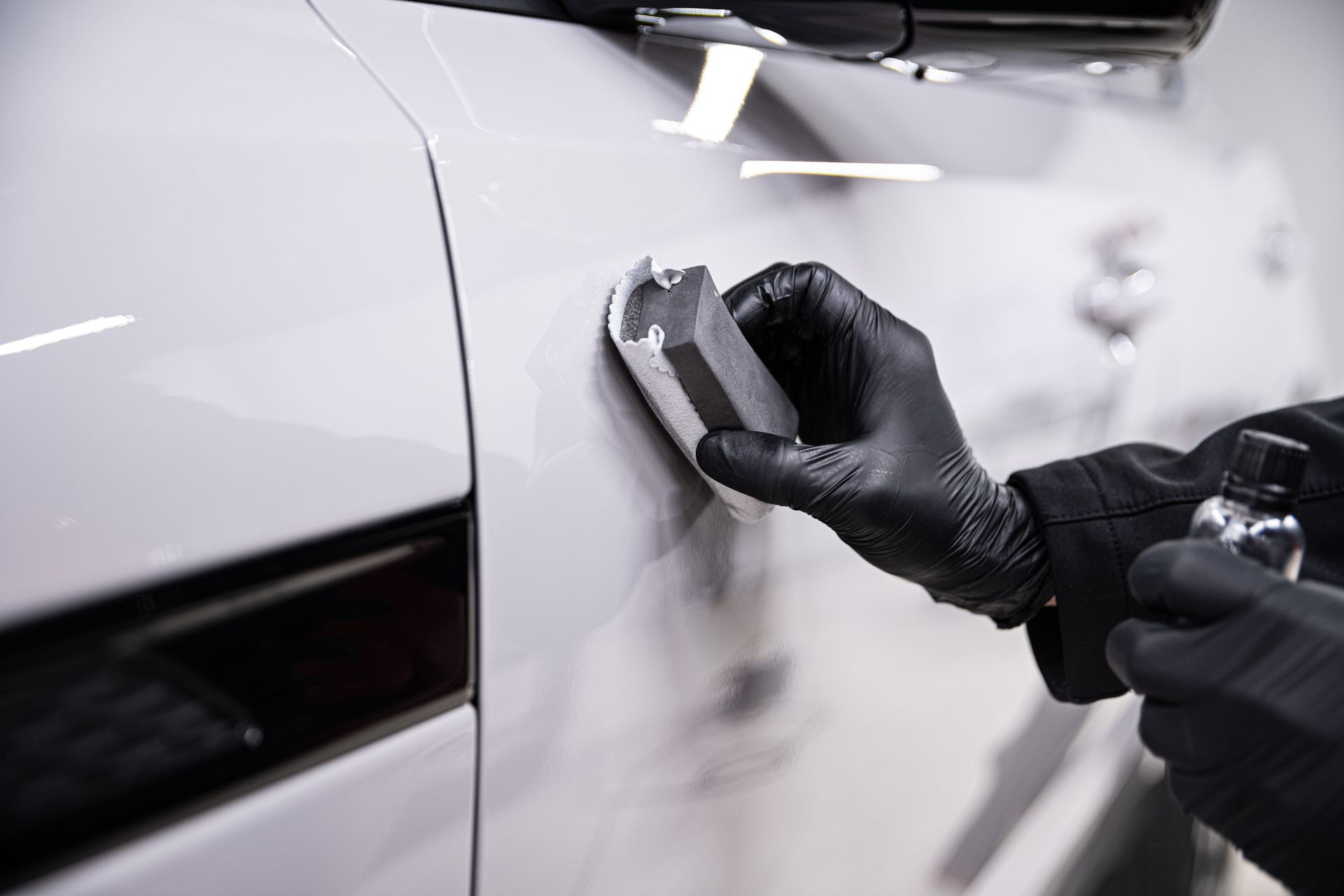 Person in black gloves applying ceramic coating to a white car.