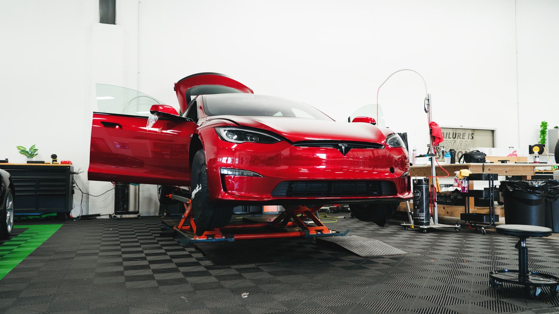 Red Tesla on a lift in a garage, doors open.