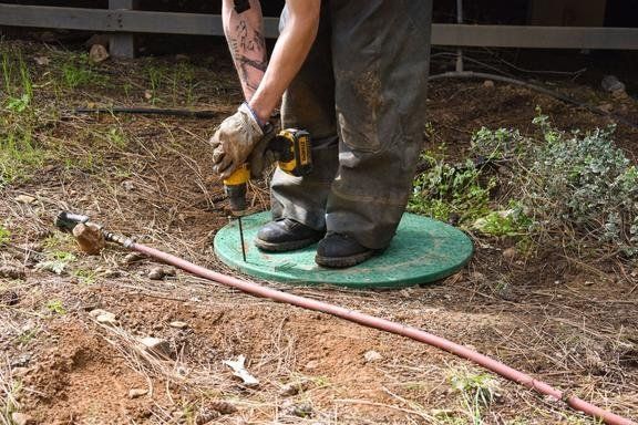 Black round utility cap with white top set in dirt beside an orange pipe and a metal post