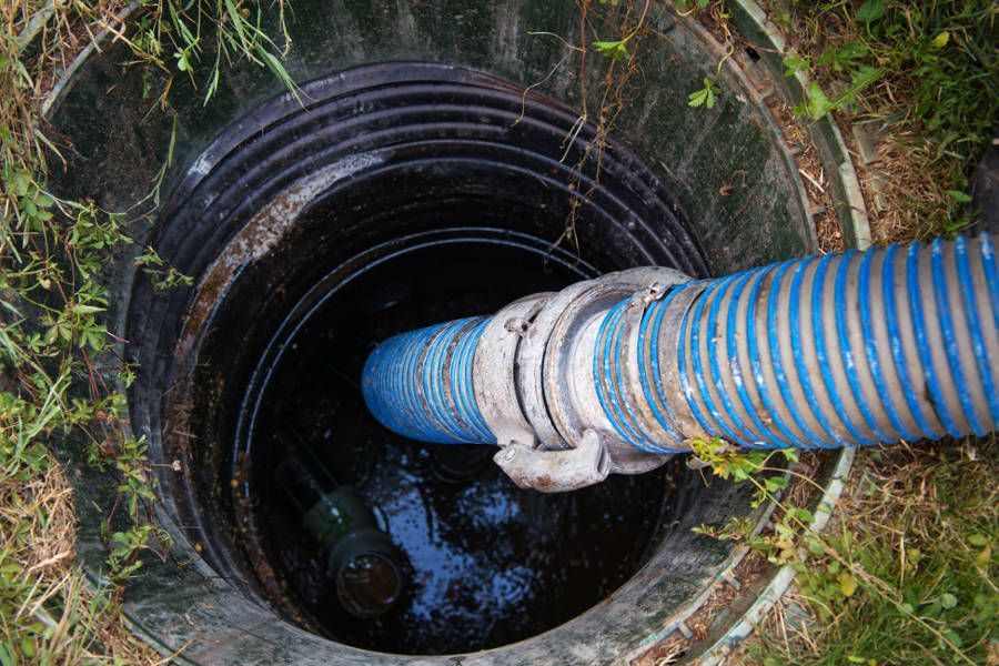 Two workers inspect an open manhole, one wearing a red helmet and one bending over the cover.