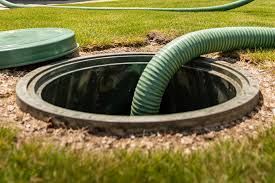 Hand lifting a green lid off a circular outdoor water tank or well opening.