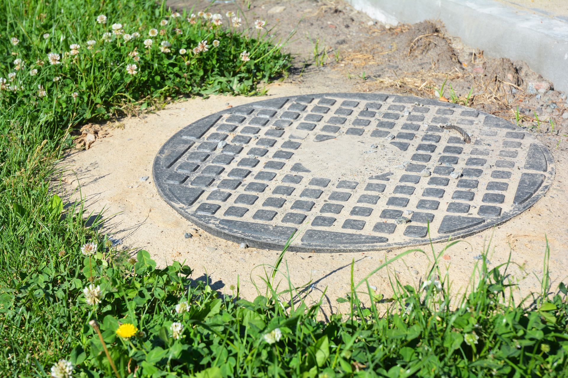 Worker in red helmet inspecting open manhole with green lid in a dirt area
