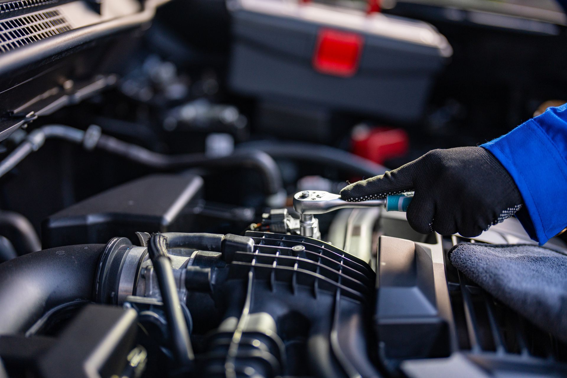 Mechanic in blue sleeve uses ratchet on car engine components.