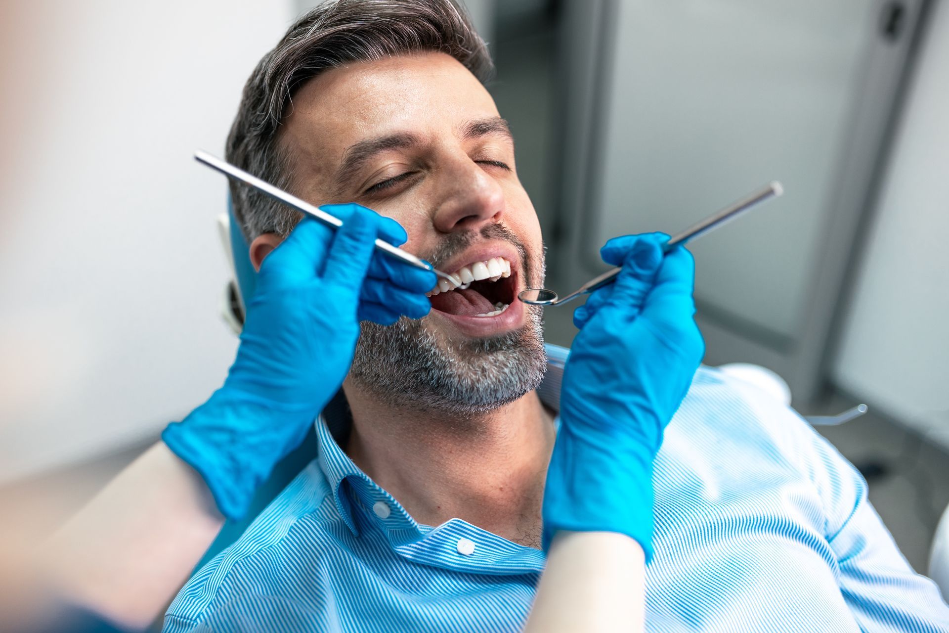 Dentist cleaning a smiling patient’s teeth with blue-gloved hands and dental tools Dentist cleaning a smiling patient’s teeth with blue-gloved hands and dental tools