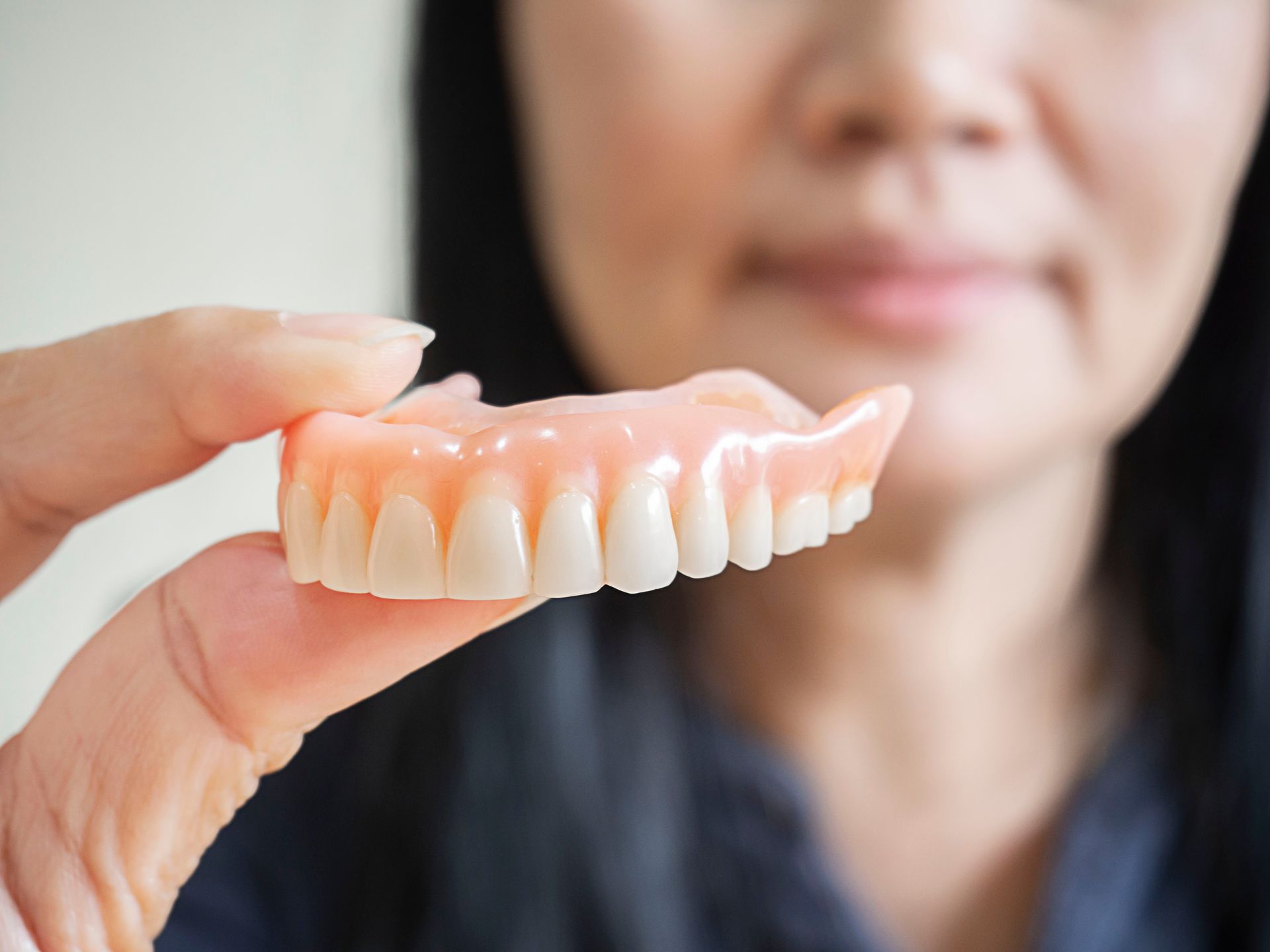 Hand holding a set of false teeth in front of a blurred person’s face