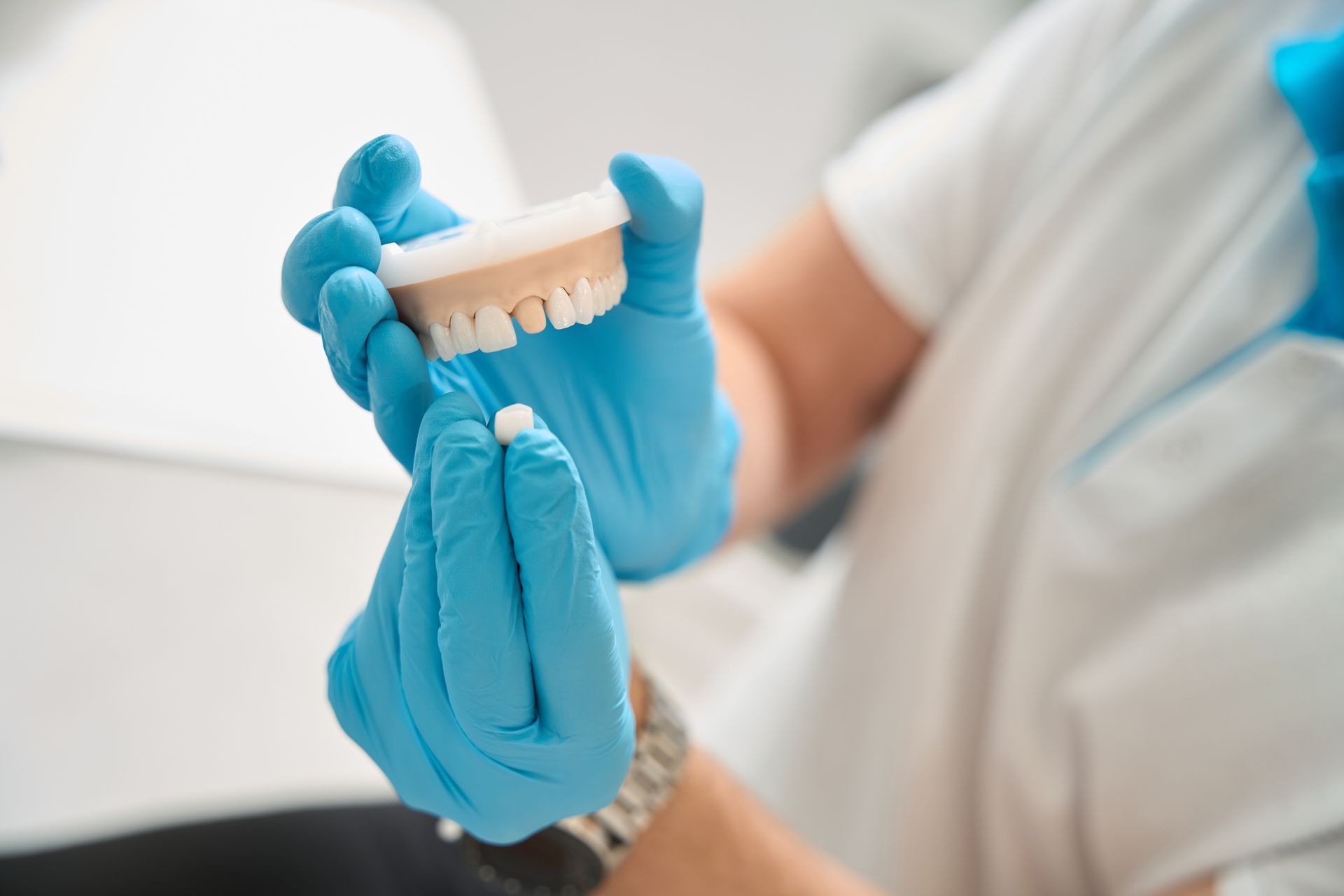 Dentist holding blue dentures with gloved hands during a dental fitting