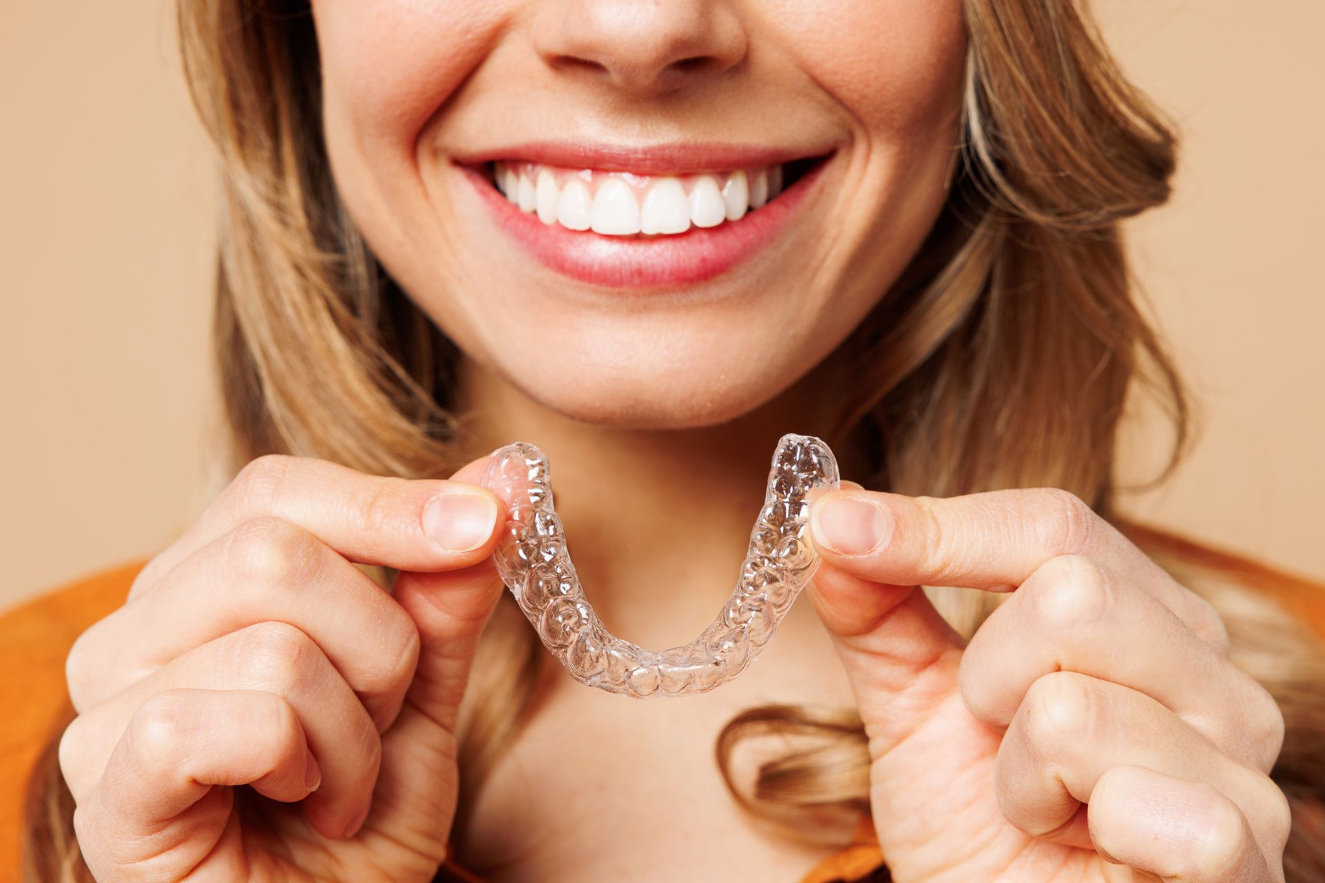 Smiling person holding a clear, U-shaped dental aligner in both hands Smiling person holding a clear, U-shaped dental aligner in both hands