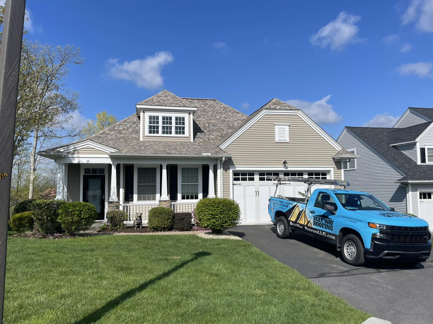 A light-colored house with a blue truck parked in the driveway on a sunny day.