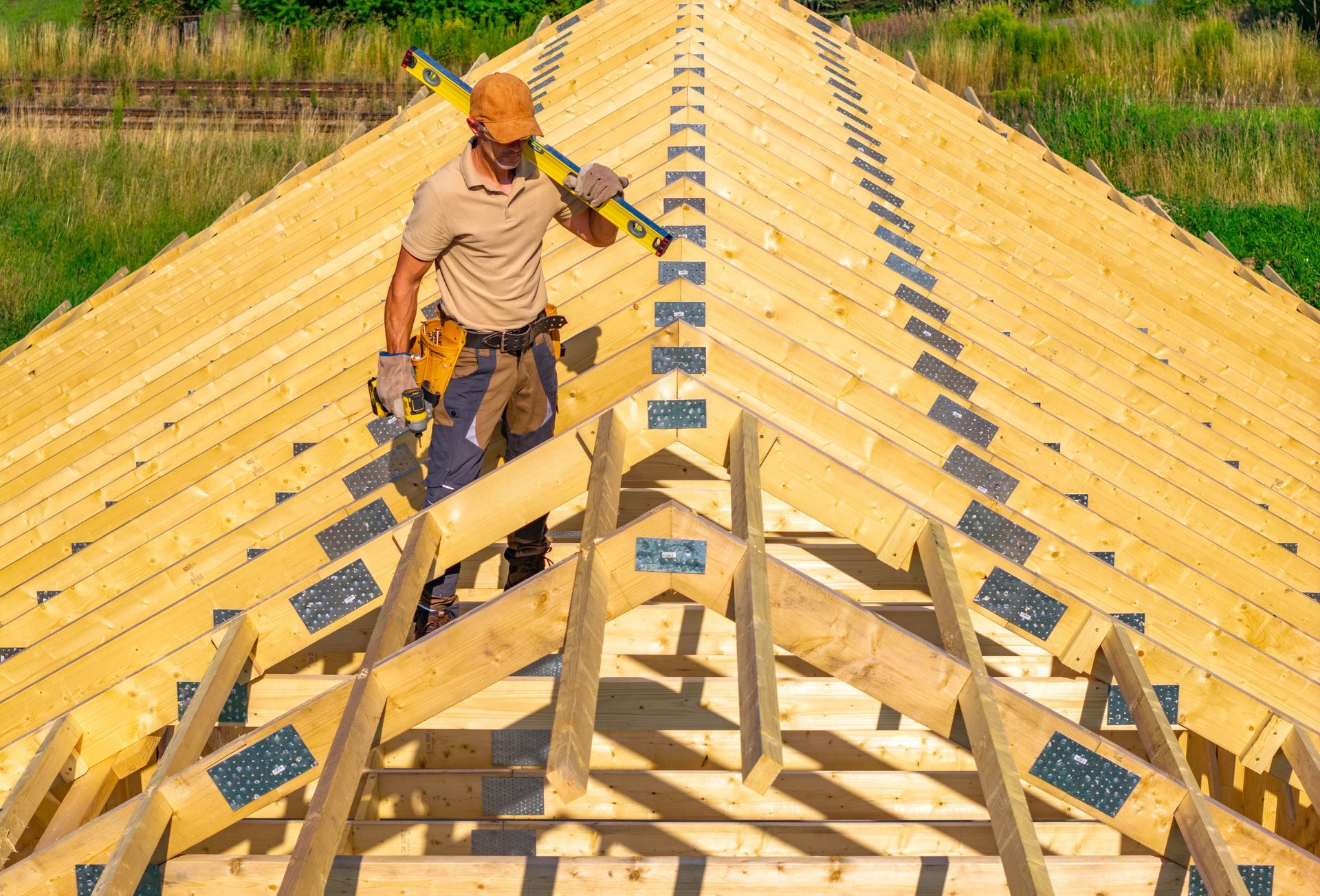 Worker standing on a wooden roof frame under construction, wearing an orange hard hat.