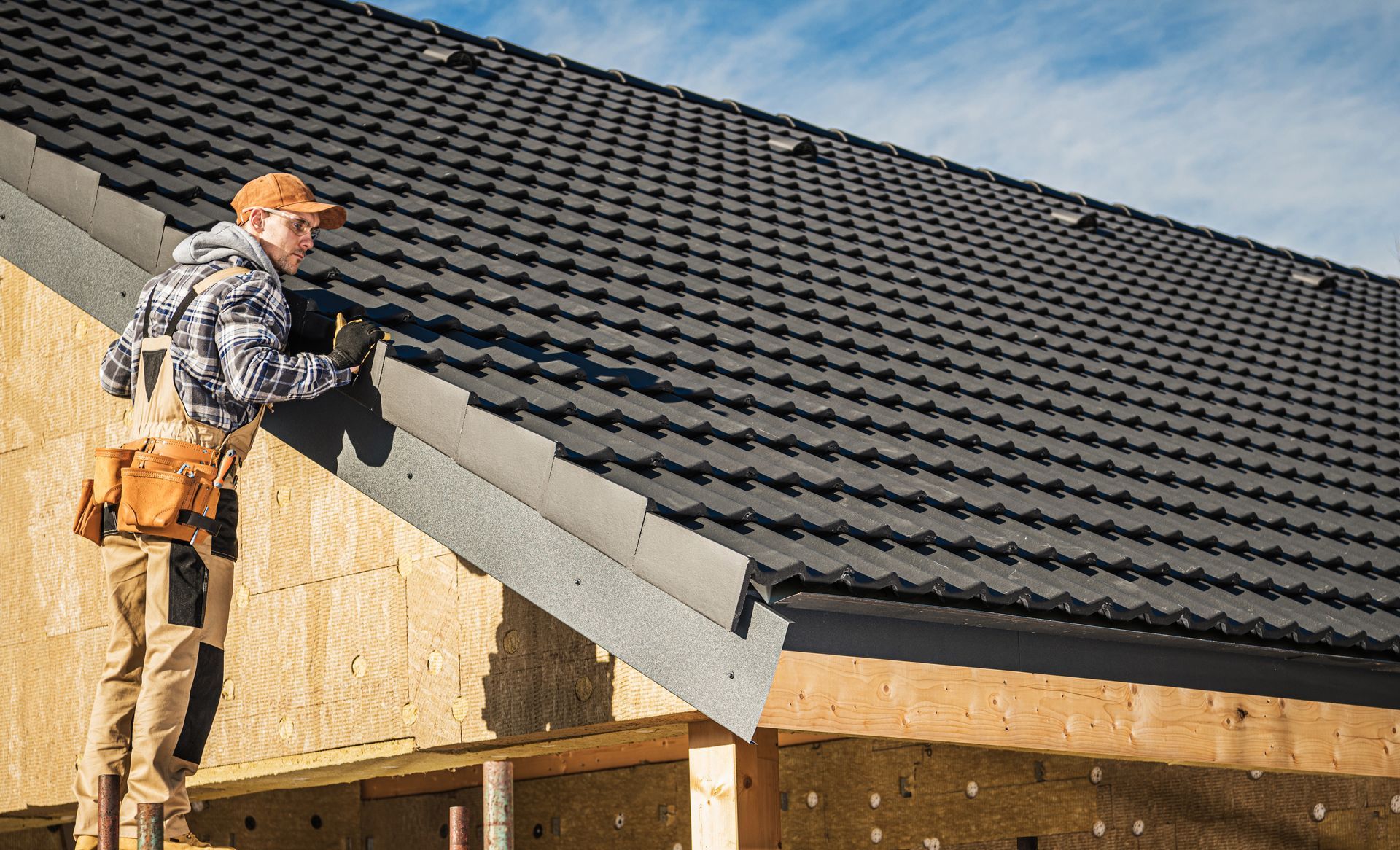Worker installing gray roof panels on a house under construction