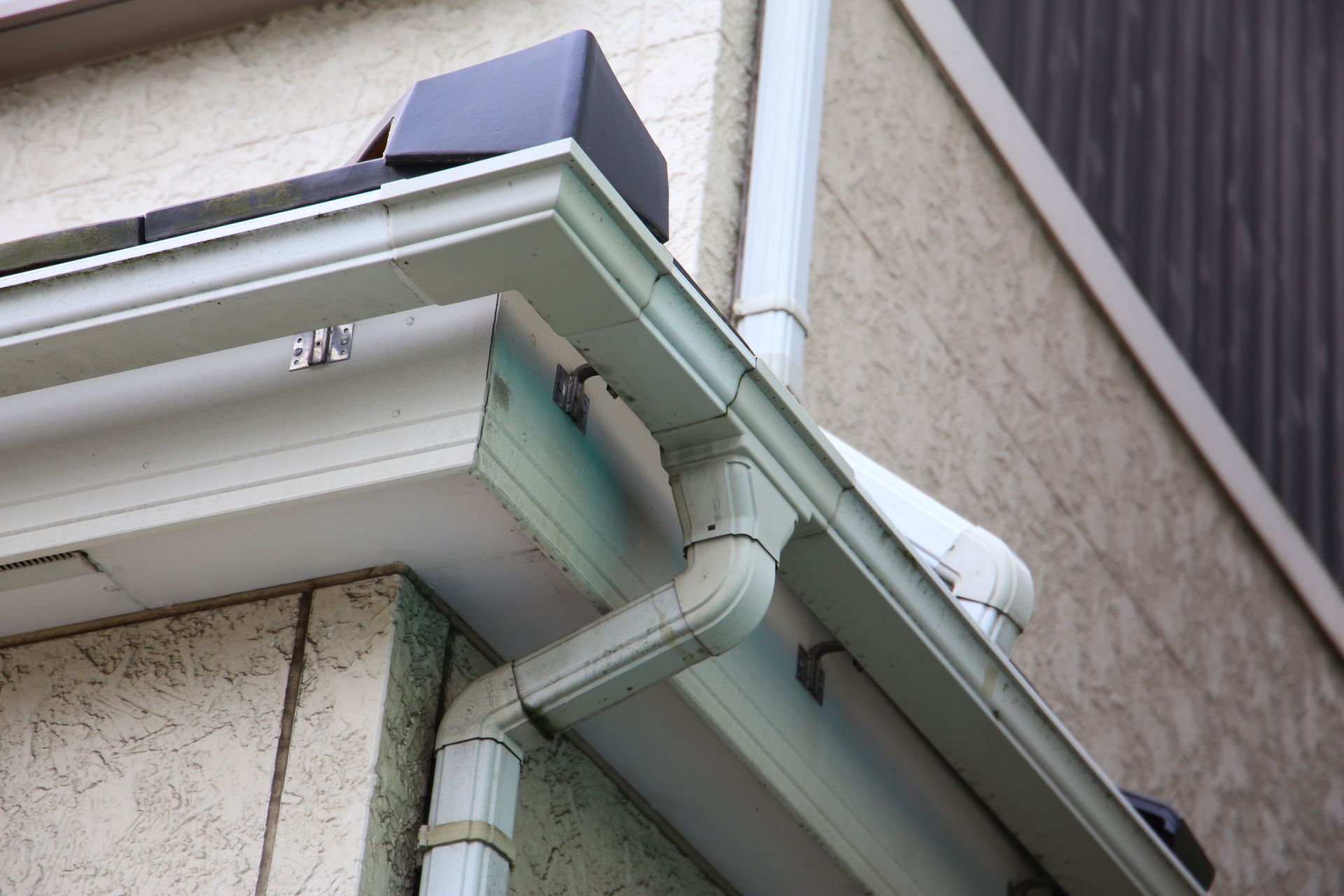 White gutter and downspout on a beige house exterior under the roof eave