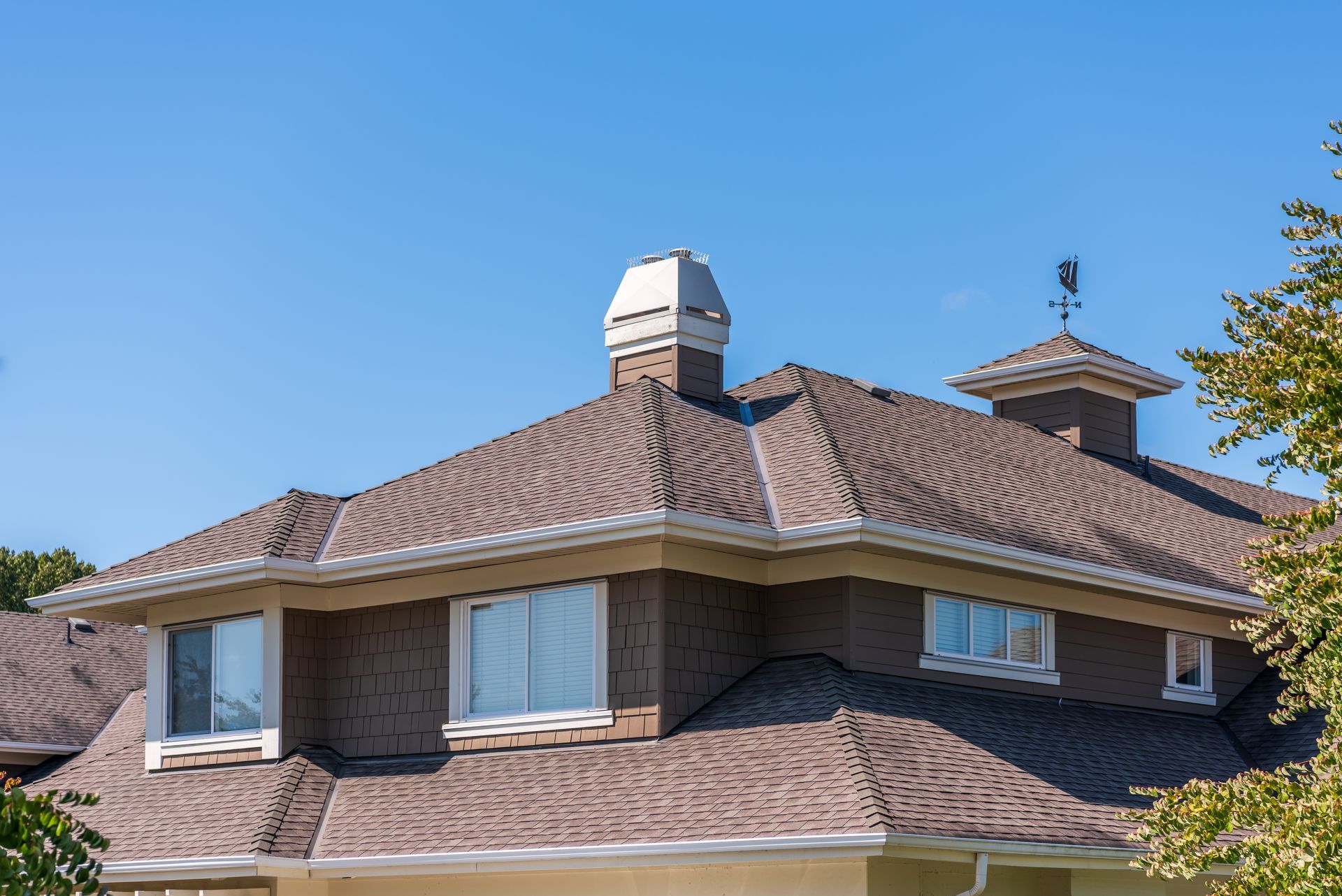 Brown tiled house roof with skylights and a vent under a clear blue sky