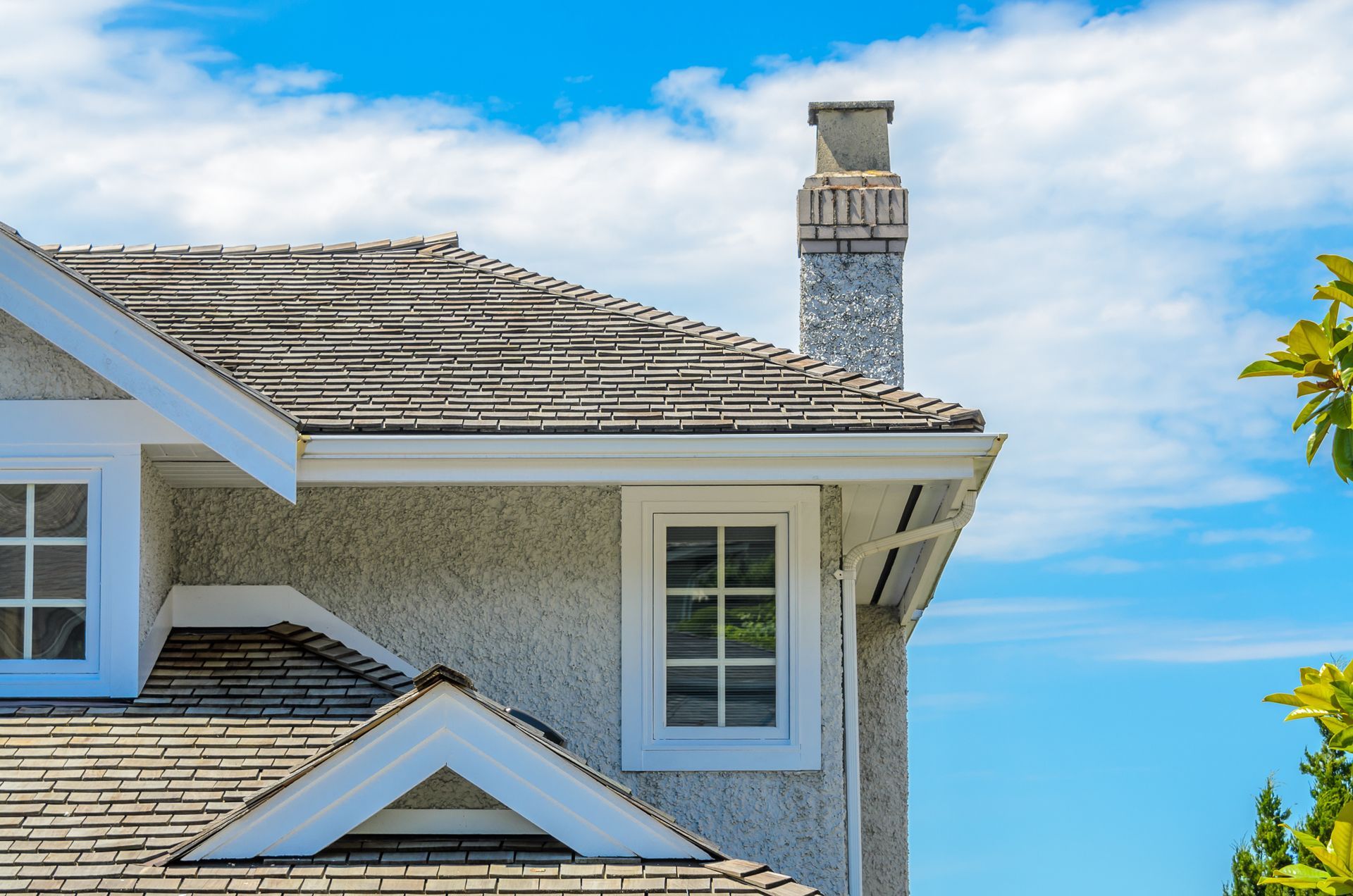Blue-gray house roof and chimney against a bright blue sky with clouds