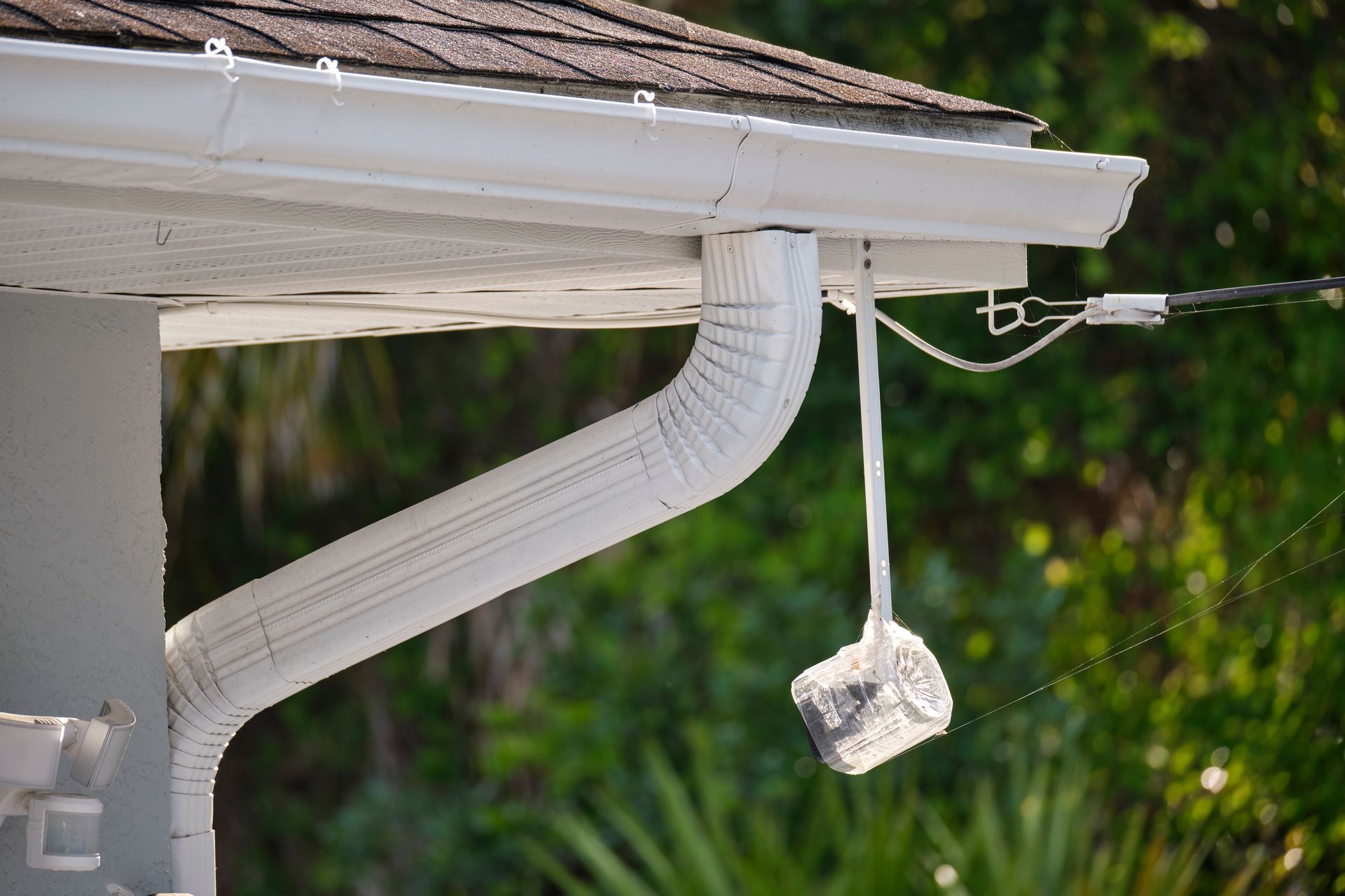 White gutter and downspout on a house roof, with a small object hanging from a cable nearby