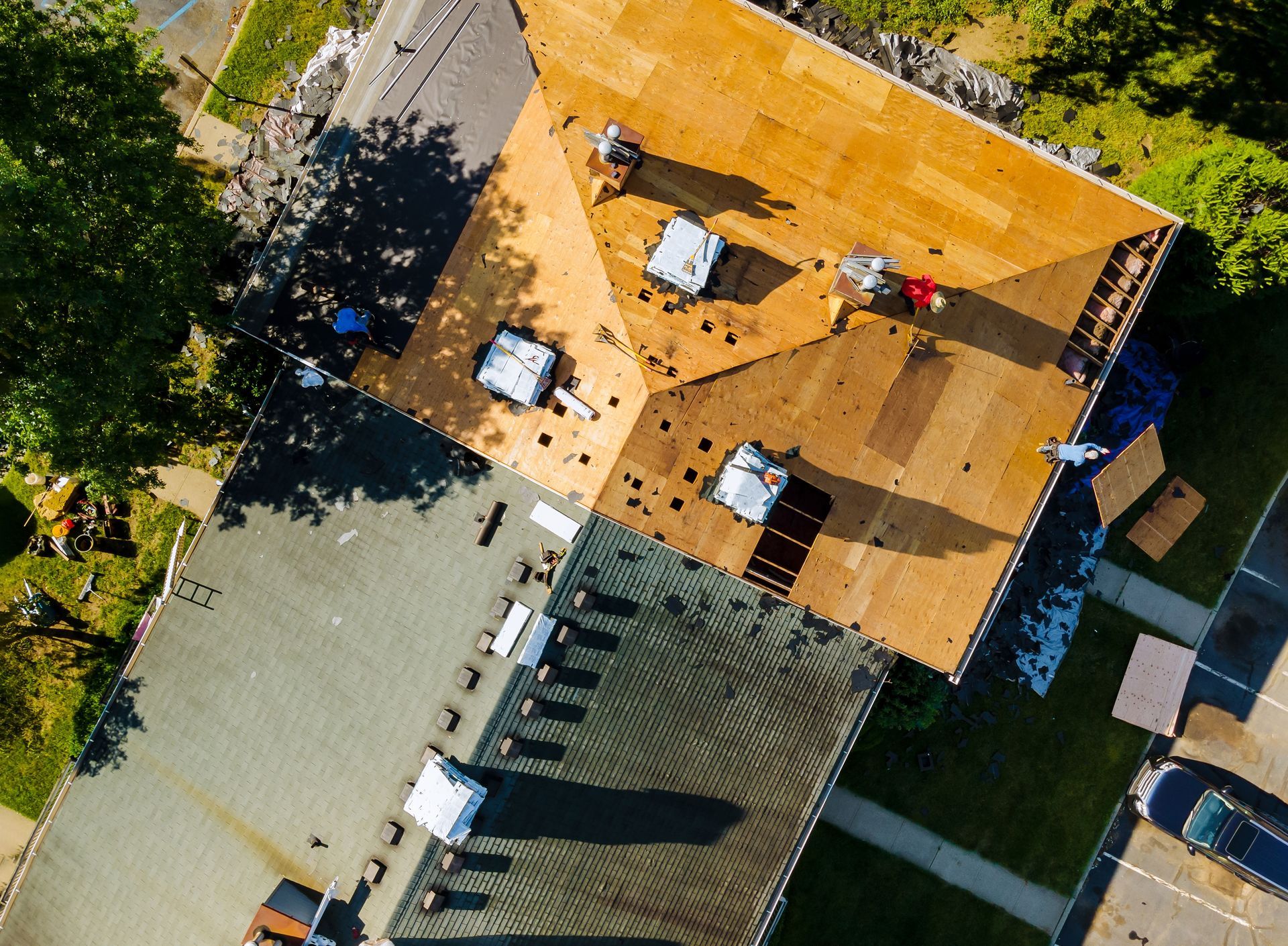 Aerial view of rooftops with solar panels, surrounded by trees and a paved area