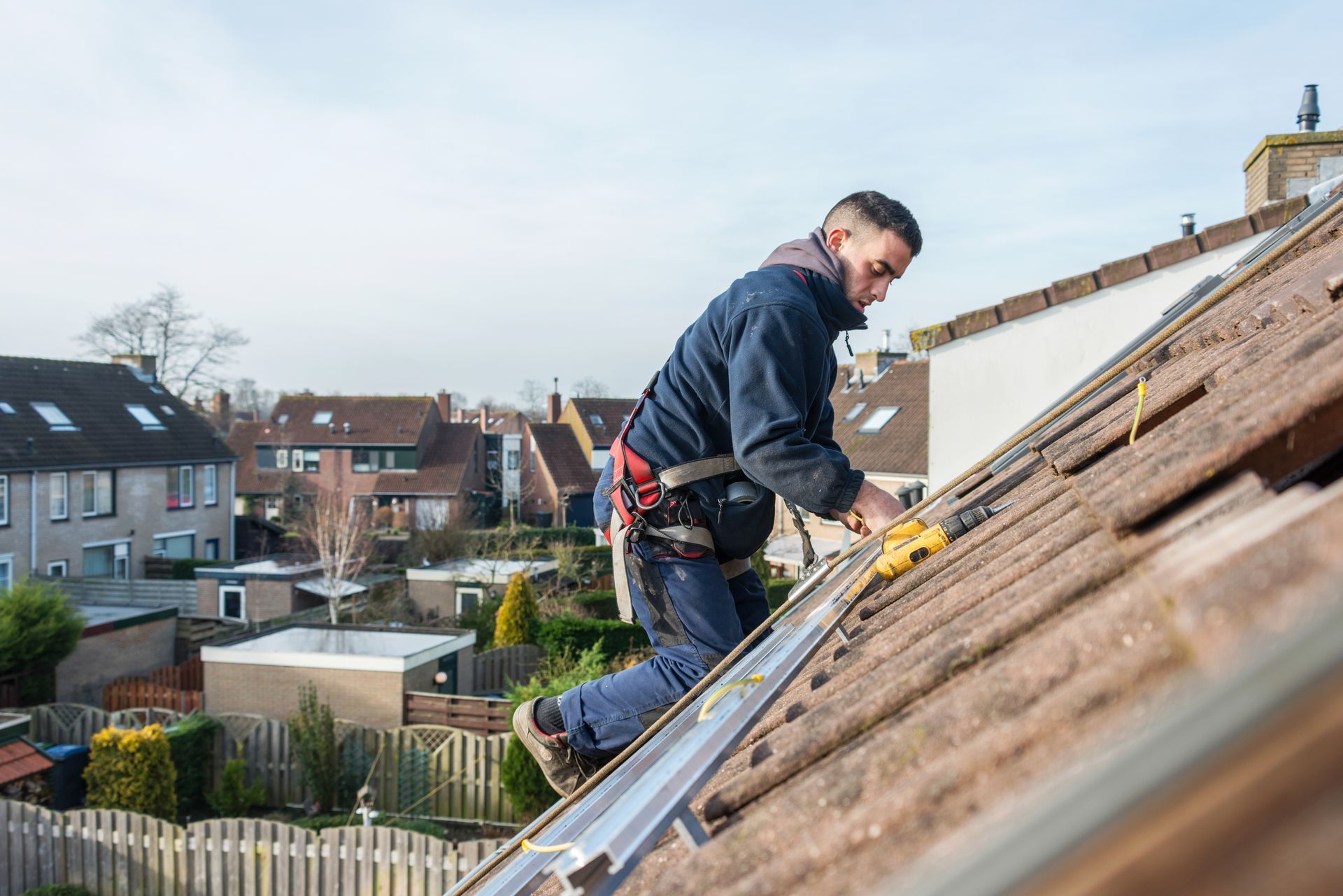 Roofer working on a sloped tile roof with a tool belt in a suburban neighborhood