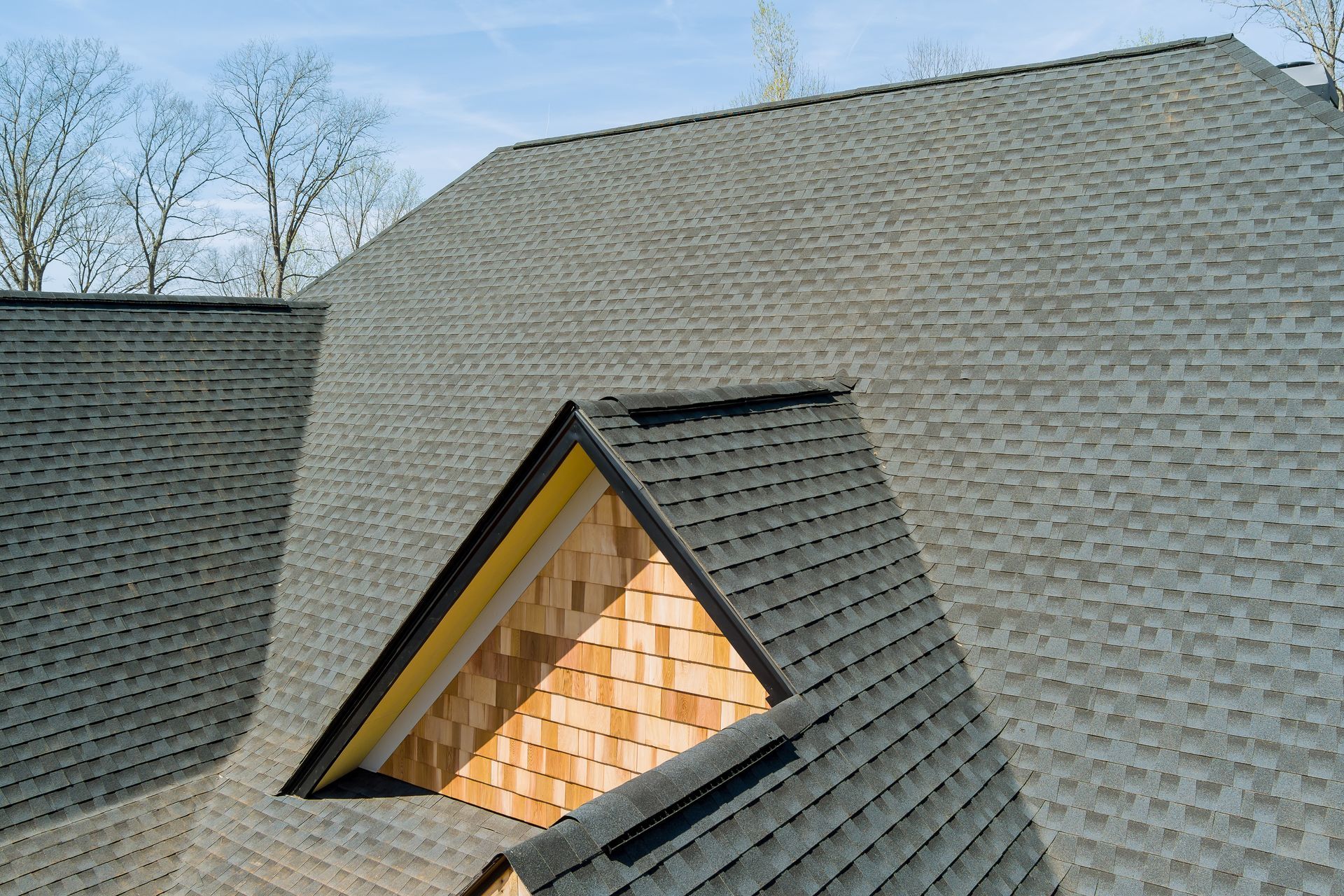 Gray shingled roof with a dormer window showing warm light inside