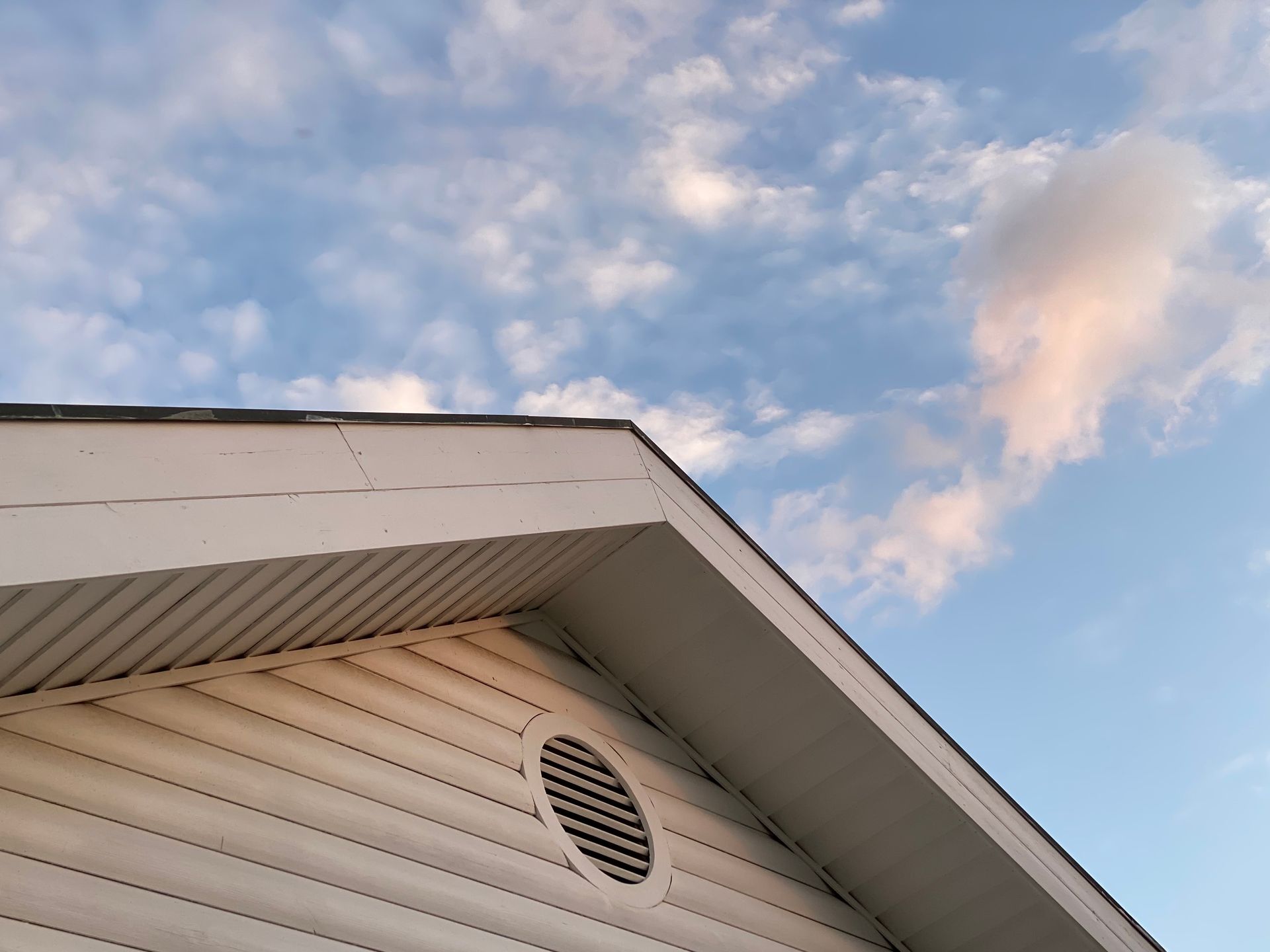 White house eaves with a round vent beneath a partly cloudy blue sky