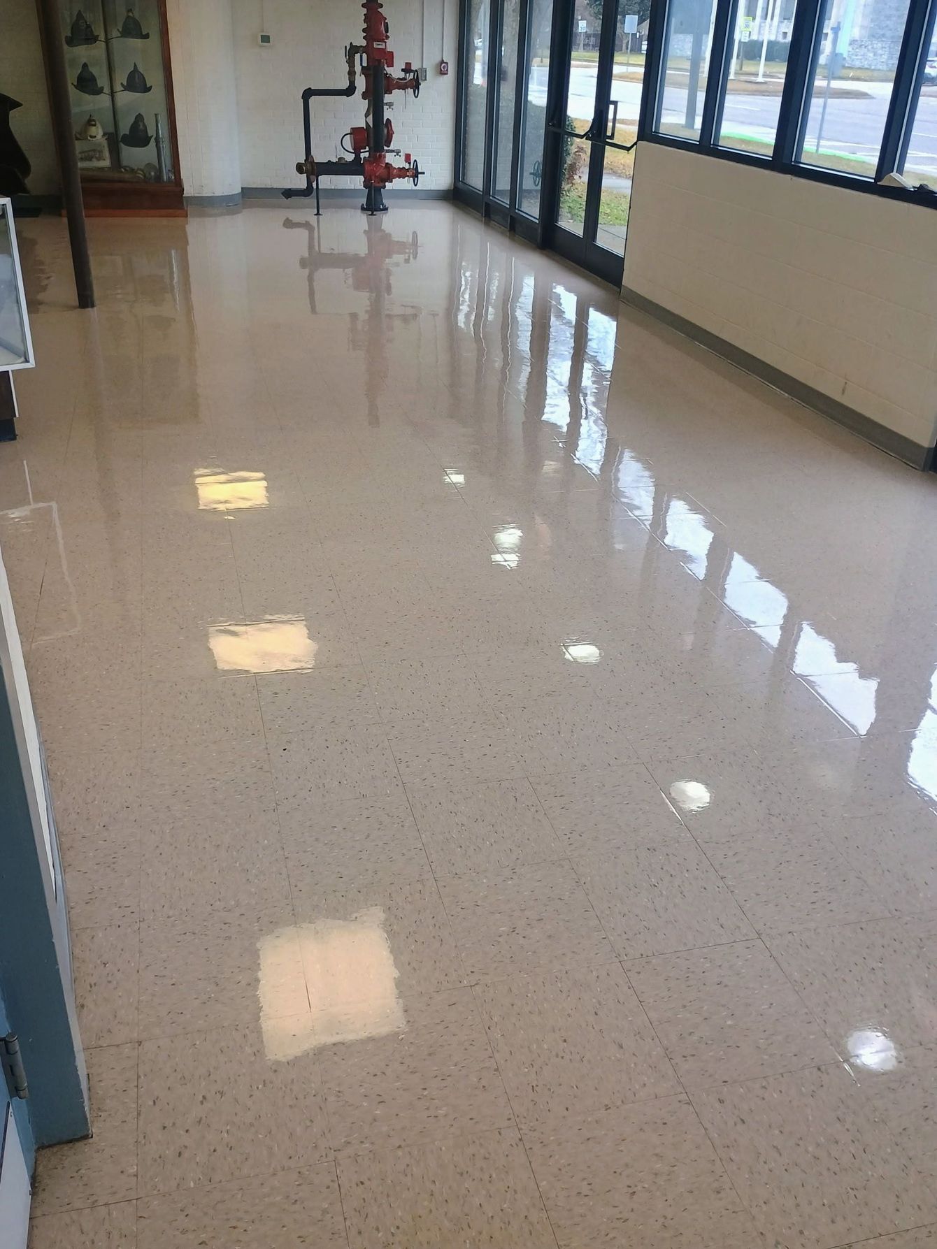 A high-gloss speckled tan floor in a hallway with windows on the right and patch repairs visible on the floor surface.