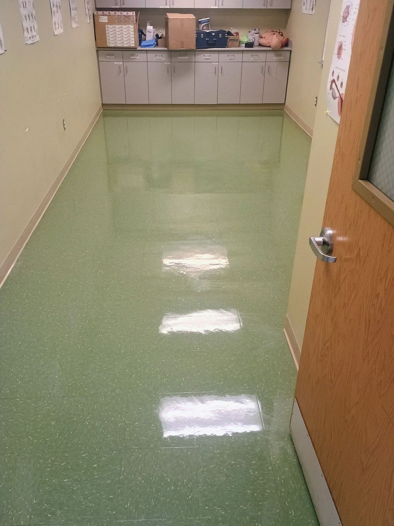 A narrow hallway with light green speckled flooring and beige walls, leading to cabinets with boxes on the counter.