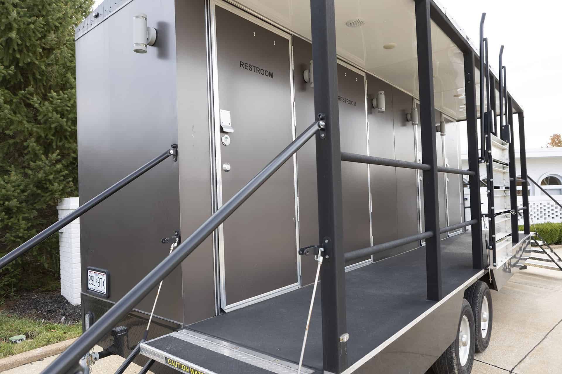 Portable black restroom trailer with accessible ramp and railings on wheels