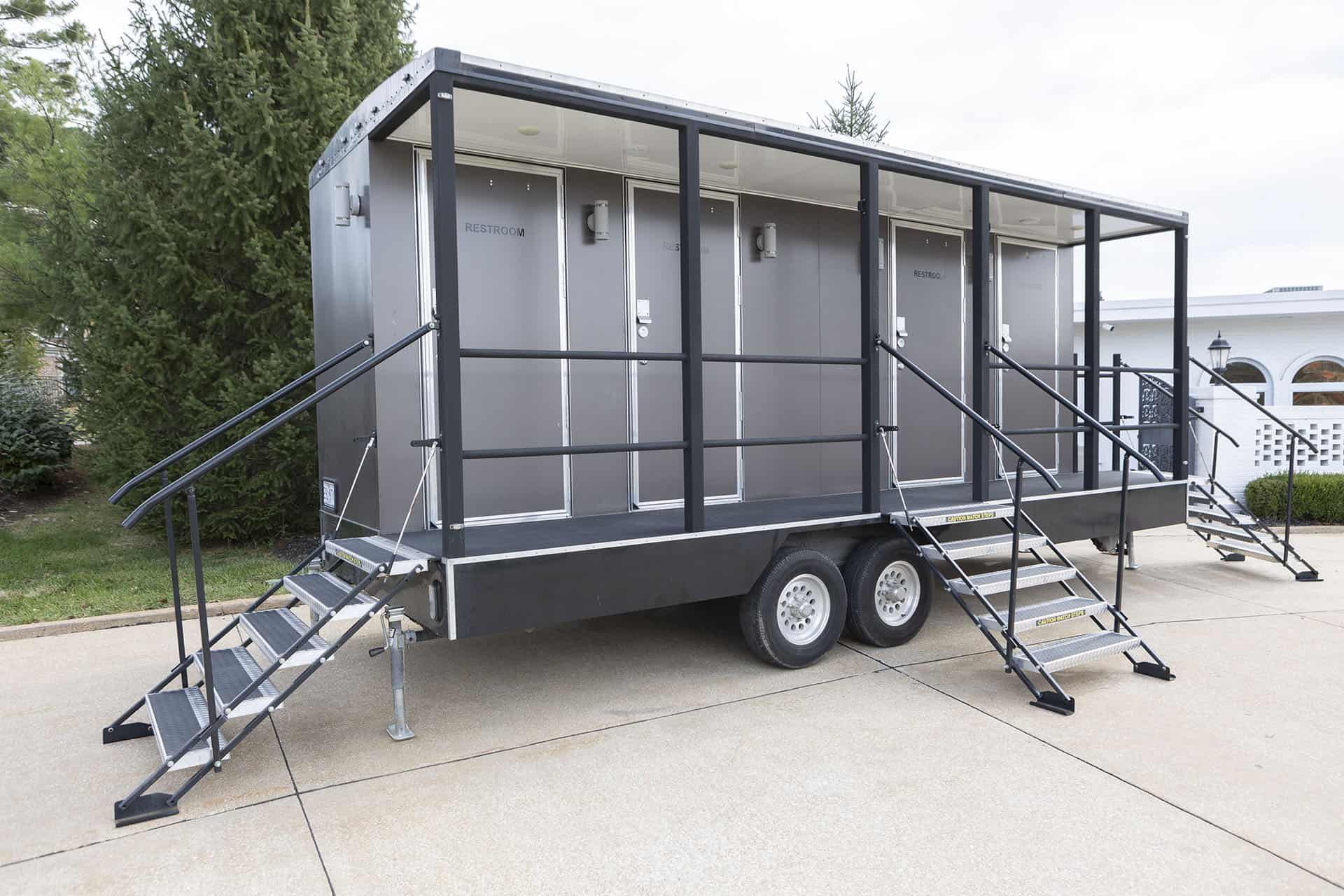 Portable gray stage trailer with stairs and railings, parked on a concrete lot outdoors