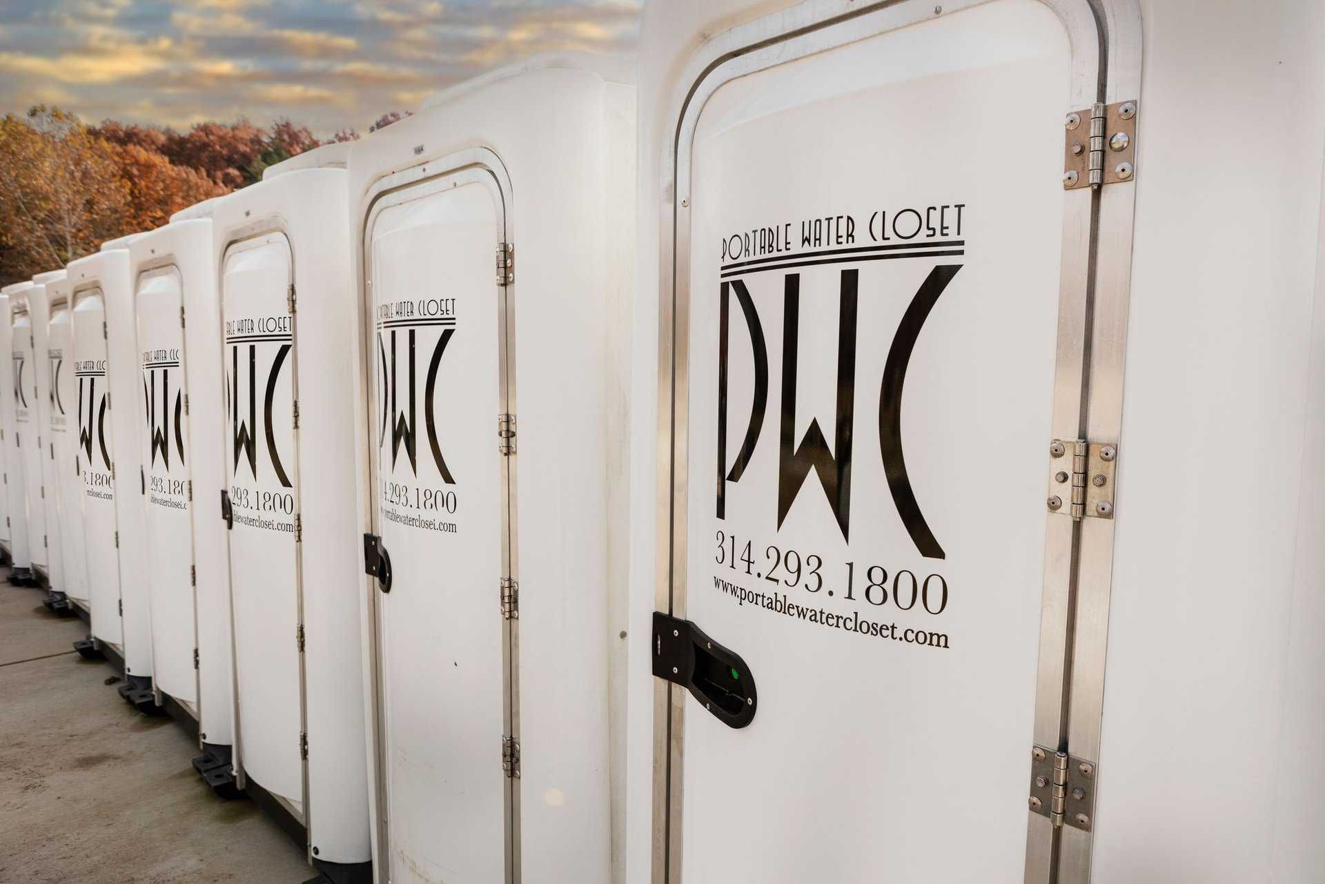 Row of white portable toilets with black logos outdoors under a cloudy sky