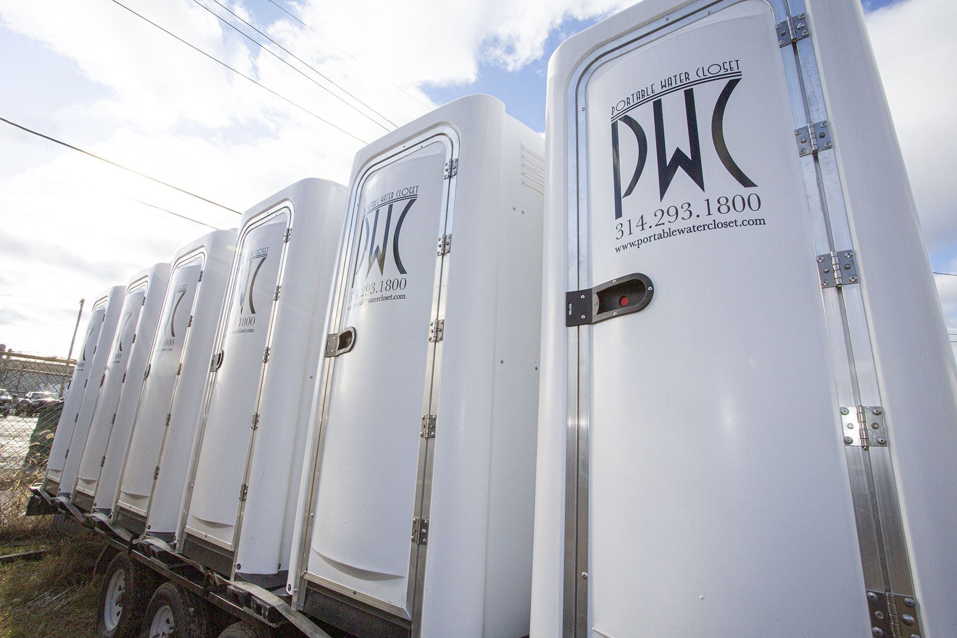 Row of white portable toilets with DWK logos outdoors under a bright sky