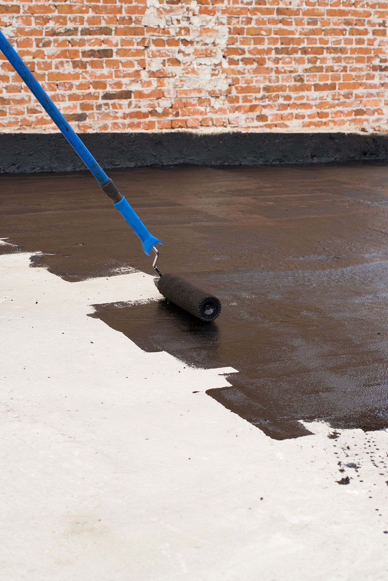 Una persona está pintando un piso de concreto con un rodillo.