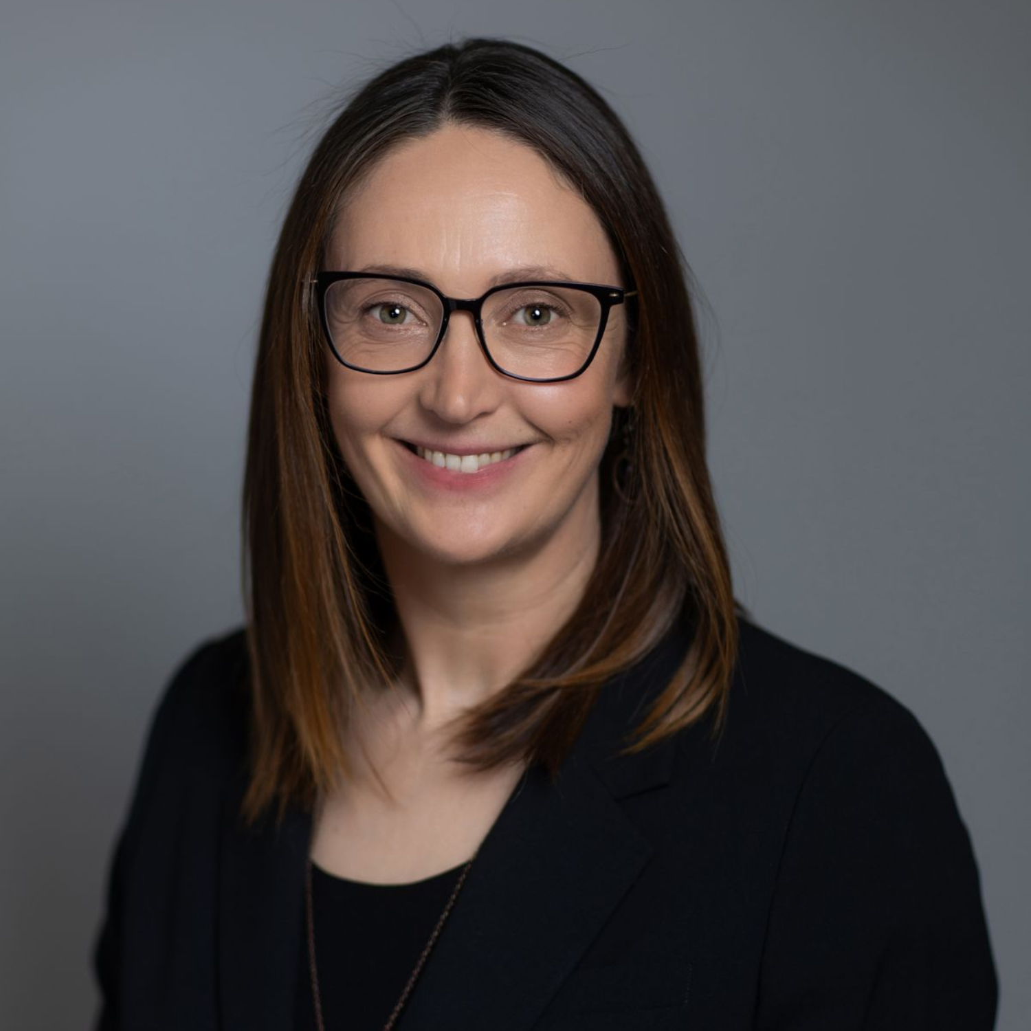 Portrait of a smiling person with glasses in a black top against a gray background