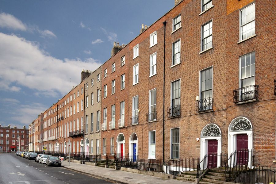 Row of red-brick townhouses on a quiet street with parked cars under a partly cloudy sky