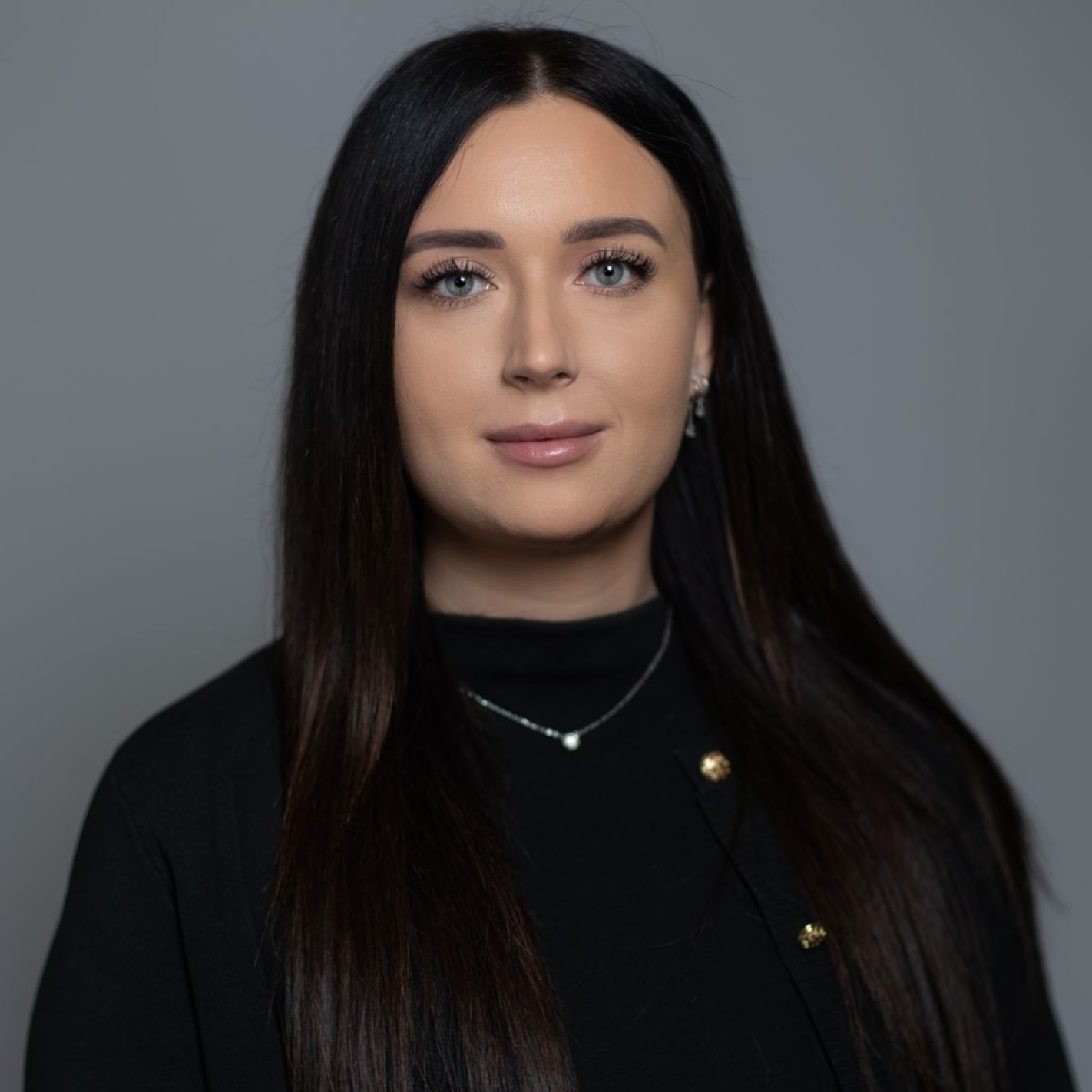 Studio portrait of a woman with long dark hair wearing a black top against a gray background
