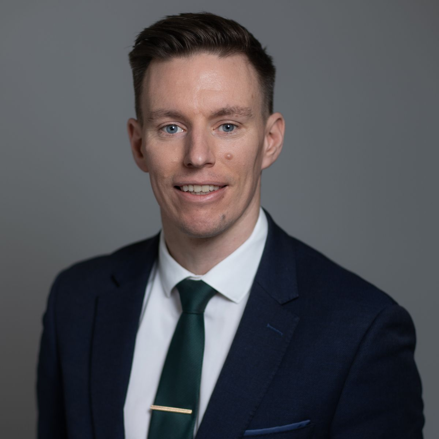 Portrait of a man in a dark suit, white shirt, and green tie against a gray background