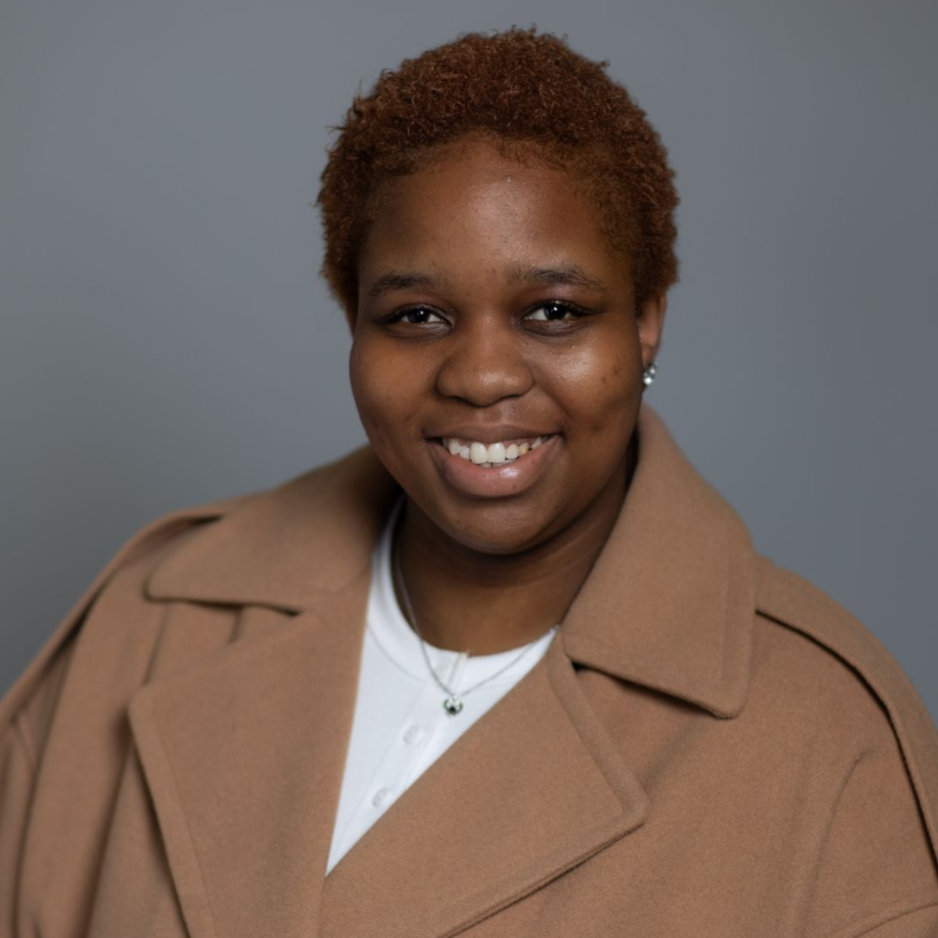 Smiling person in a tan coat against a gray background