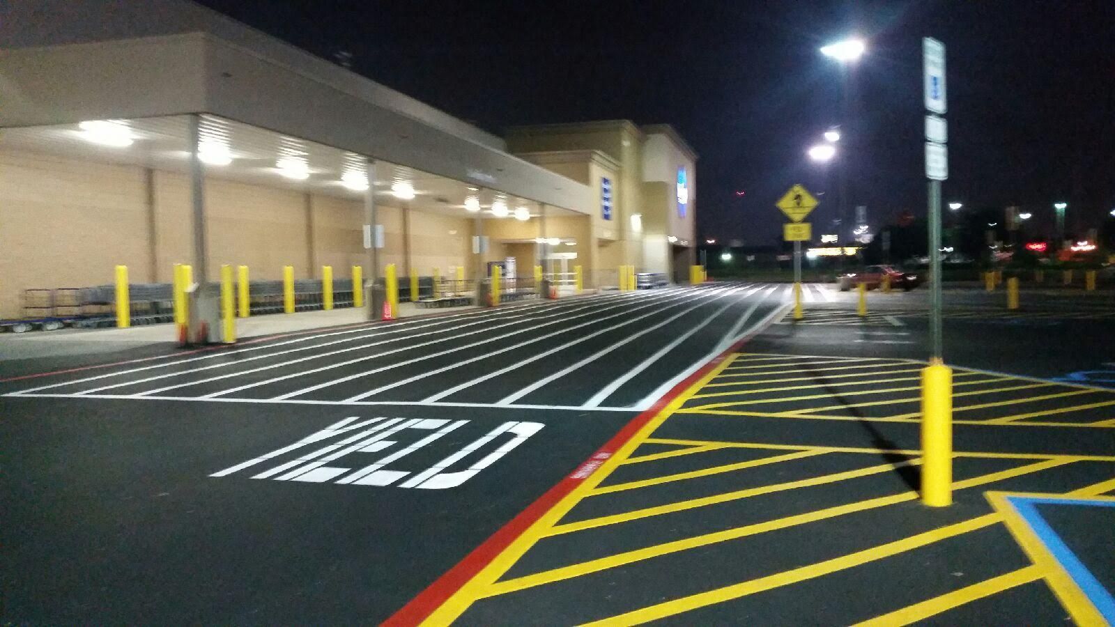 Empty store parking lot at night with yellow bollards, red curb line, and marked crosswalk lanes.