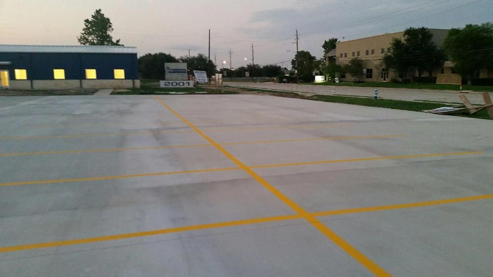 Empty concrete parking lot with yellow lines at dusk, buildings in the background.
