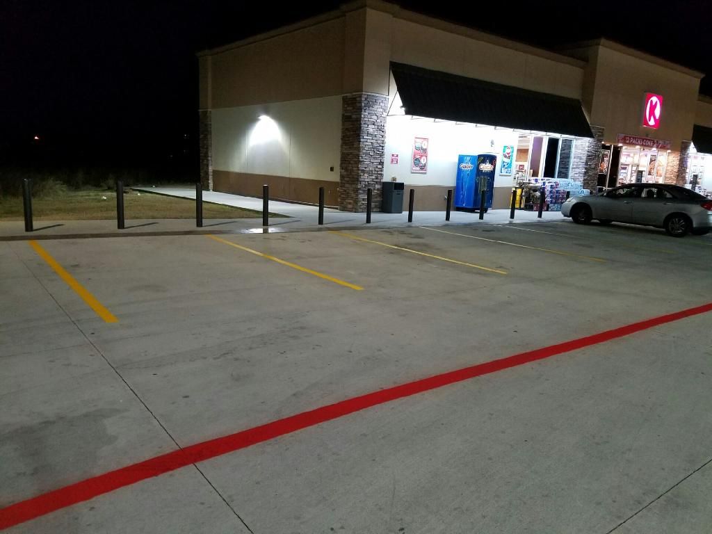 Nighttime convenience store parking lot with a lit storefront, blue vending machines, and parked car.