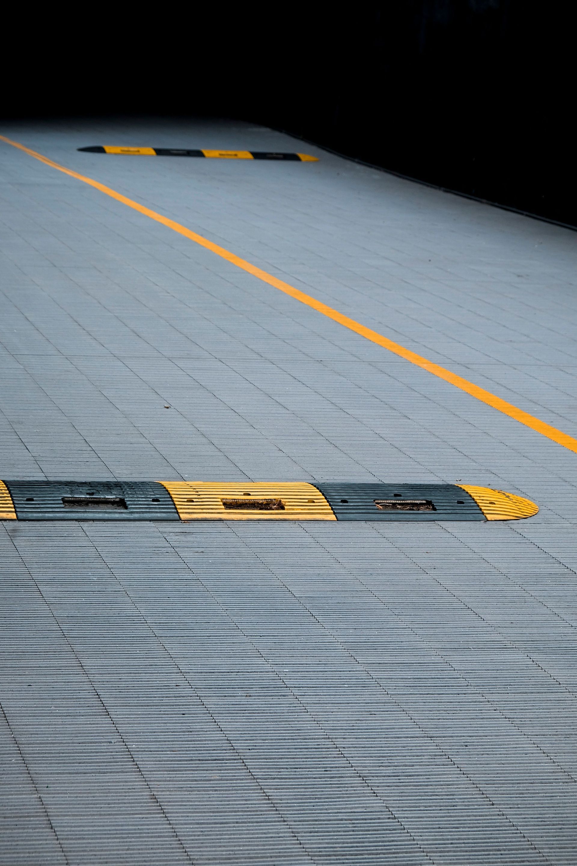 Yellow line and black-and-yellow speed bumps on a gray paved ramp or road