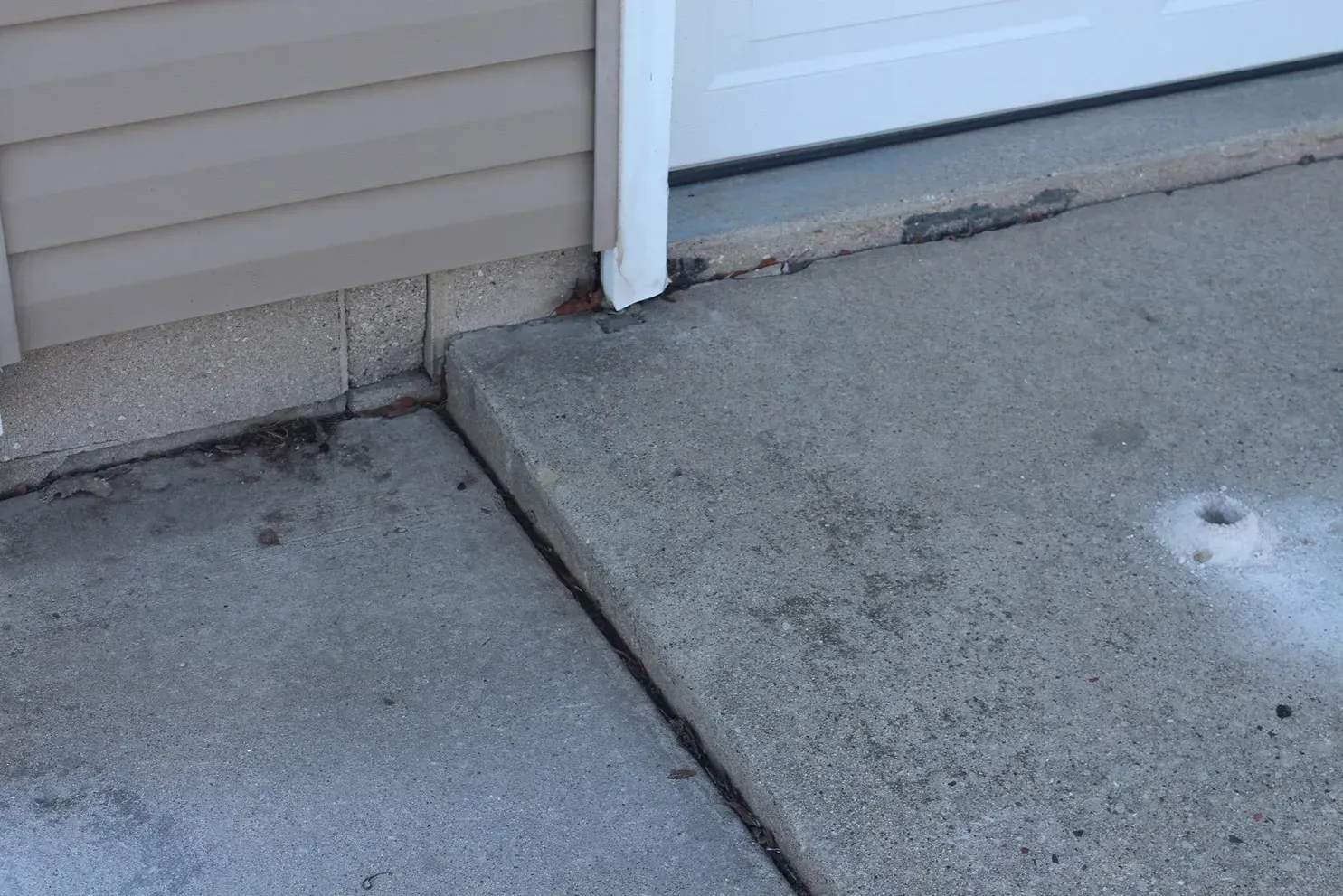Concrete sidewalk meeting a garage threshold with a visible crack and dark stain marks