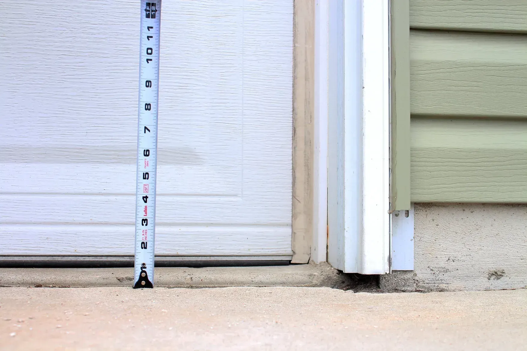 Tape measure against a garage door and siding beside a concrete driveway