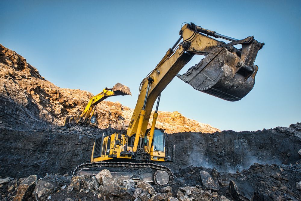 Yellow Excavator Digging in a Dark Rocky Area Under a Blue Sky — Blue Diesel & Equipment In Speewah, QLD