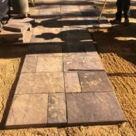 A stone walkway being constructed with rectangular pavers of varying brown and gray tones set on a sand base.