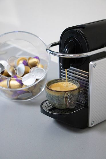 Koffiezetapparaat dat espresso in een gebloemd kopje zet; koffiecapsules liggen ernaast in een doorzichtige kom.