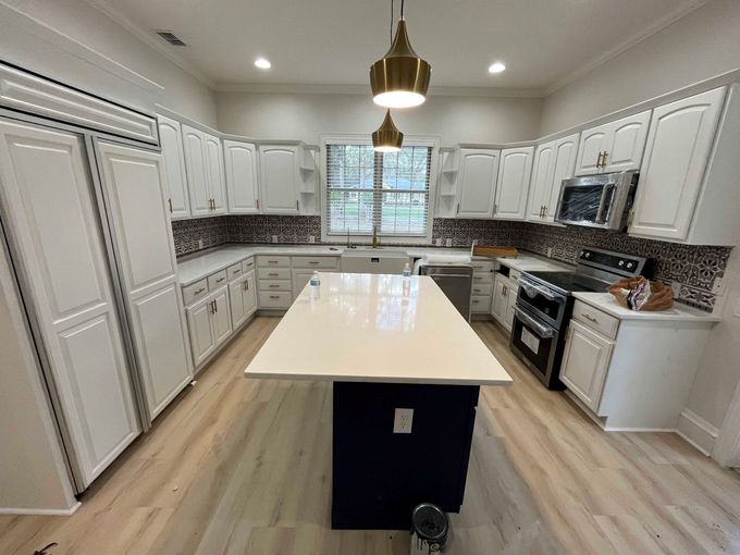 Bright modern kitchen with white cabinets, large island, stainless appliances, and wood floors