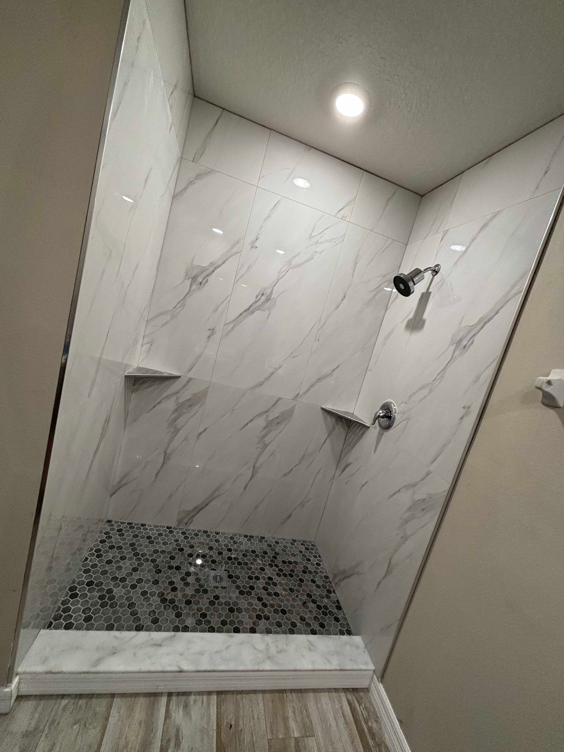 Modern tiled shower with marble-look walls, dark pebble floor, and two wall-mounted showerheads