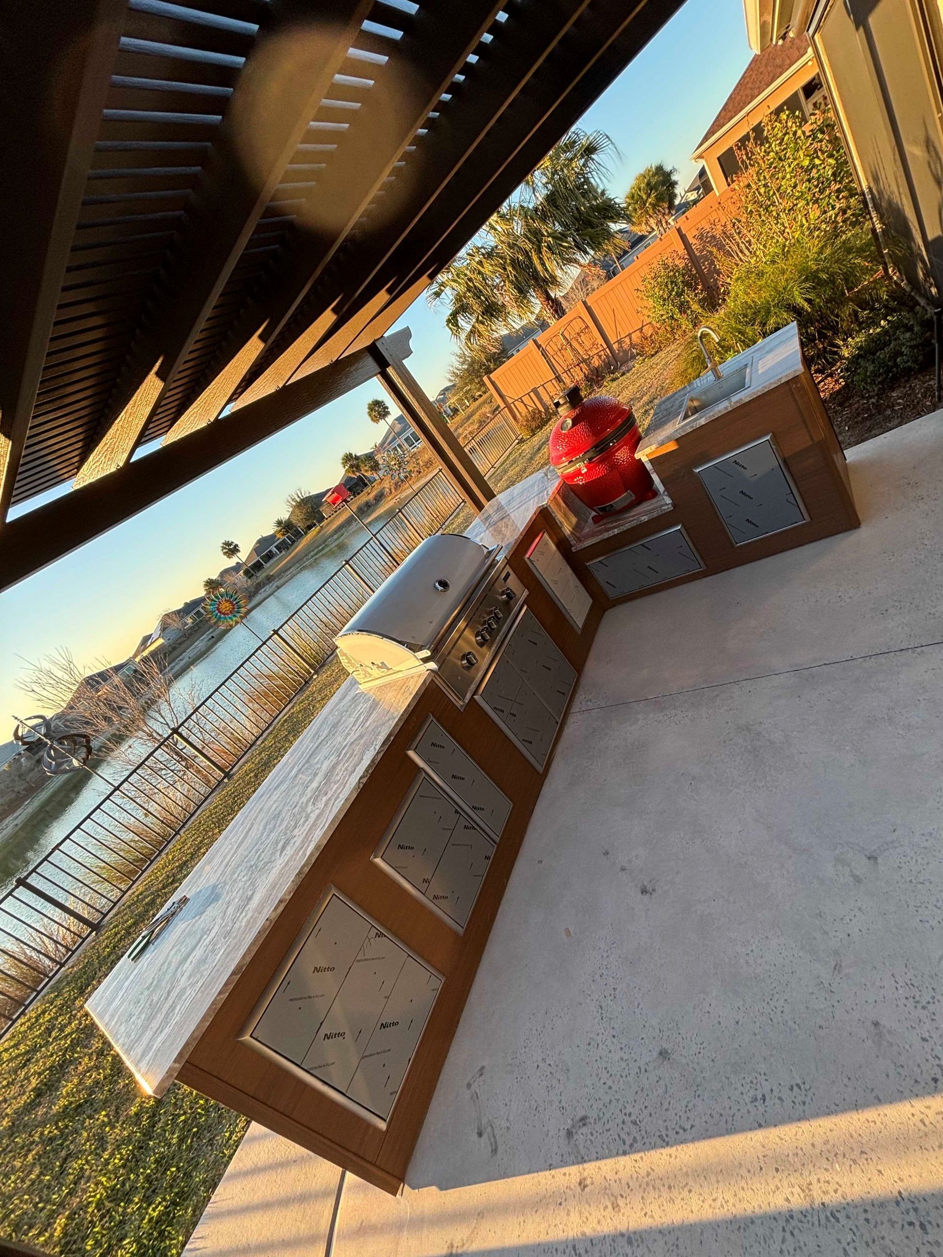 Outdoor poolside lounge with wicker chairs, a person in a red shirt, and a view of the water at sunset