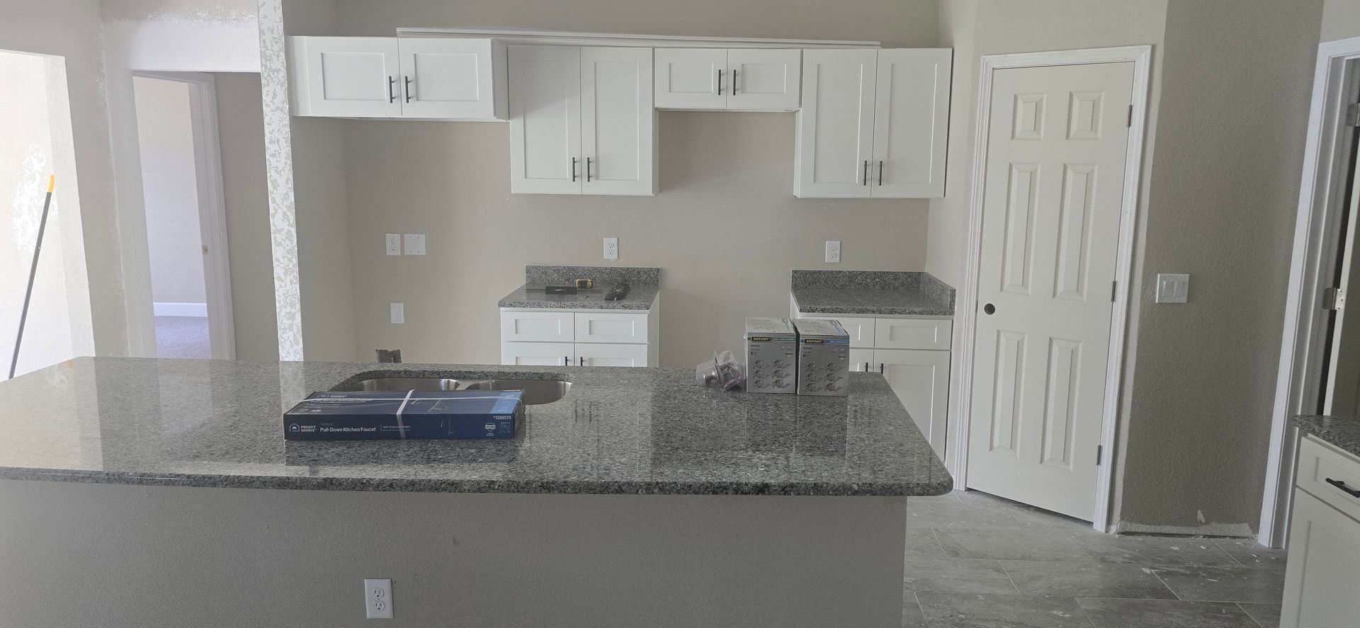 Empty kitchen with white cabinets, granite island, stove, and tiled floor.